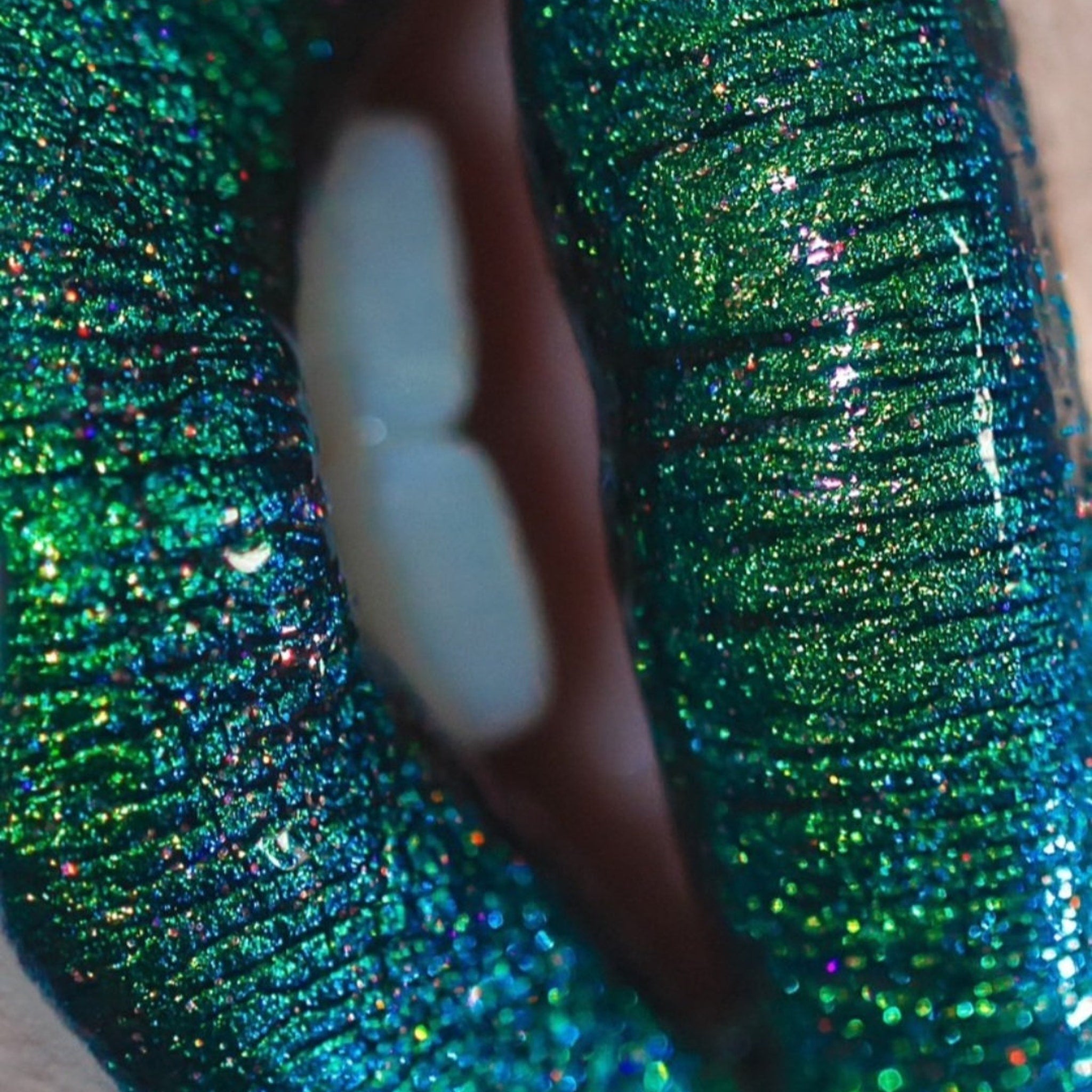 Side angle view of loose multi-chrome eye shadow pigment catching light with shimmering color shift effect