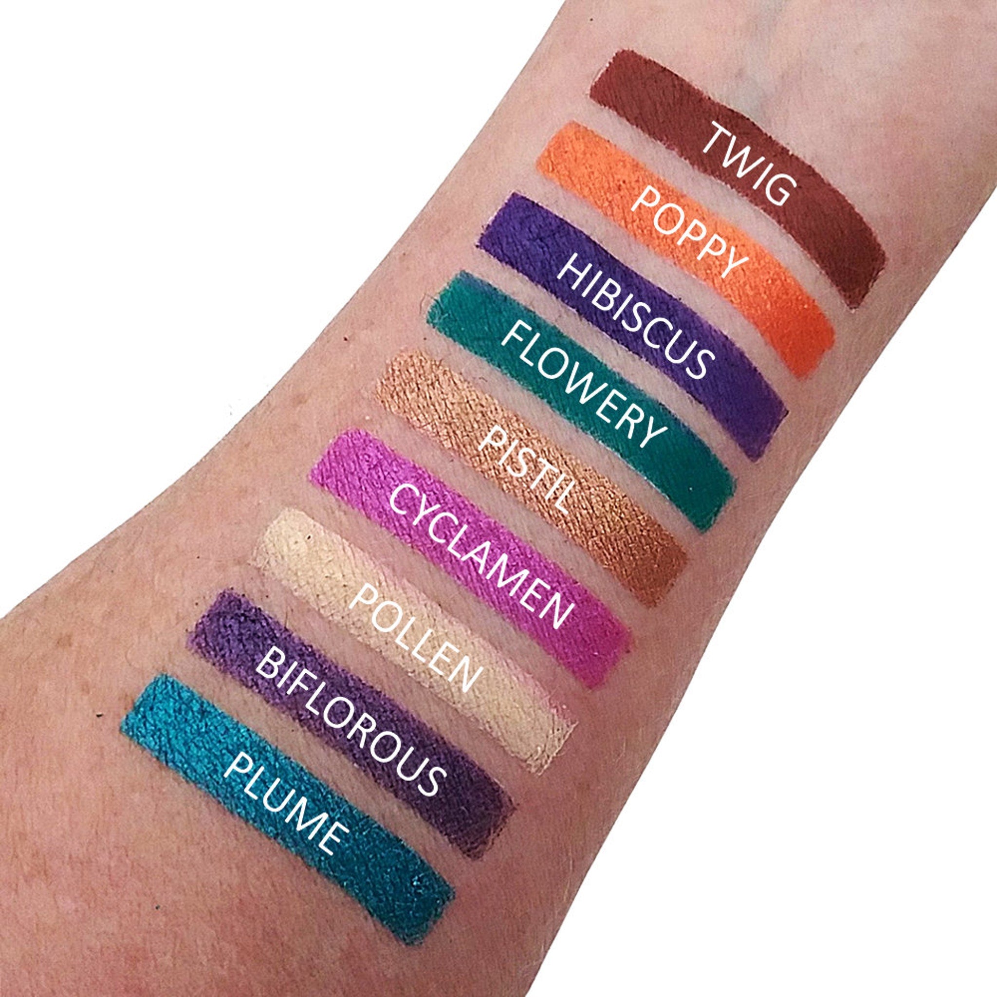Swatches of eyeshadow colors in various shades on skin, with color names visible in white text