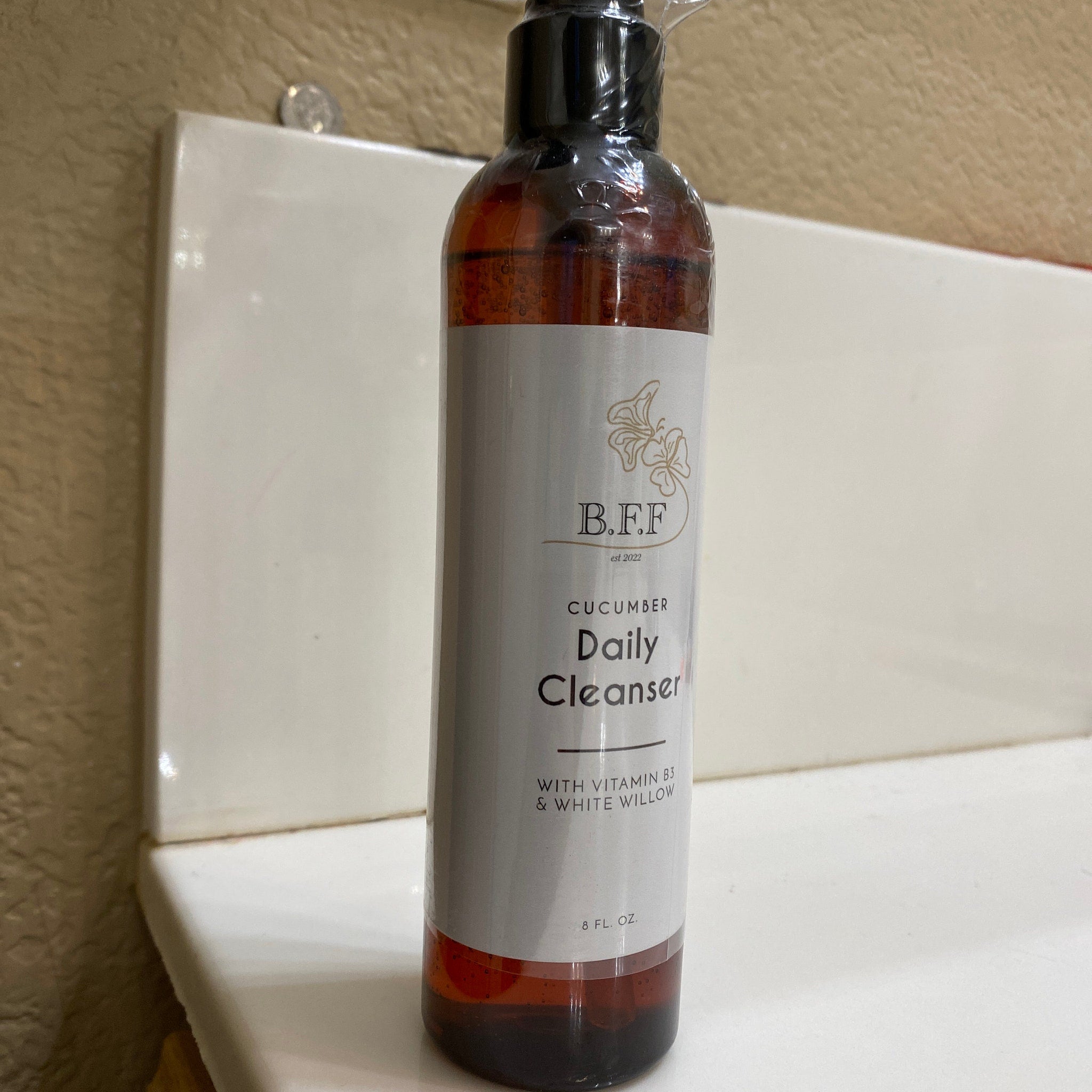 Daily cleanser bottle with brown liquid, white label, and black cap, B.F.F. branding visible.