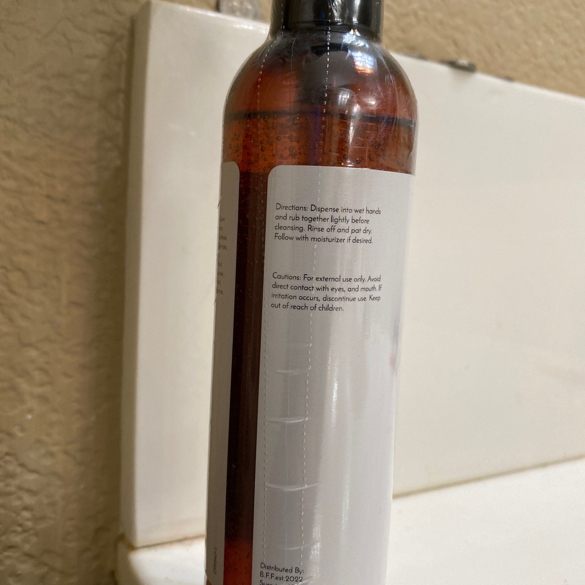 Brown liquid bottle with white label, clear plastic wrap, and black cap, for cleansing use