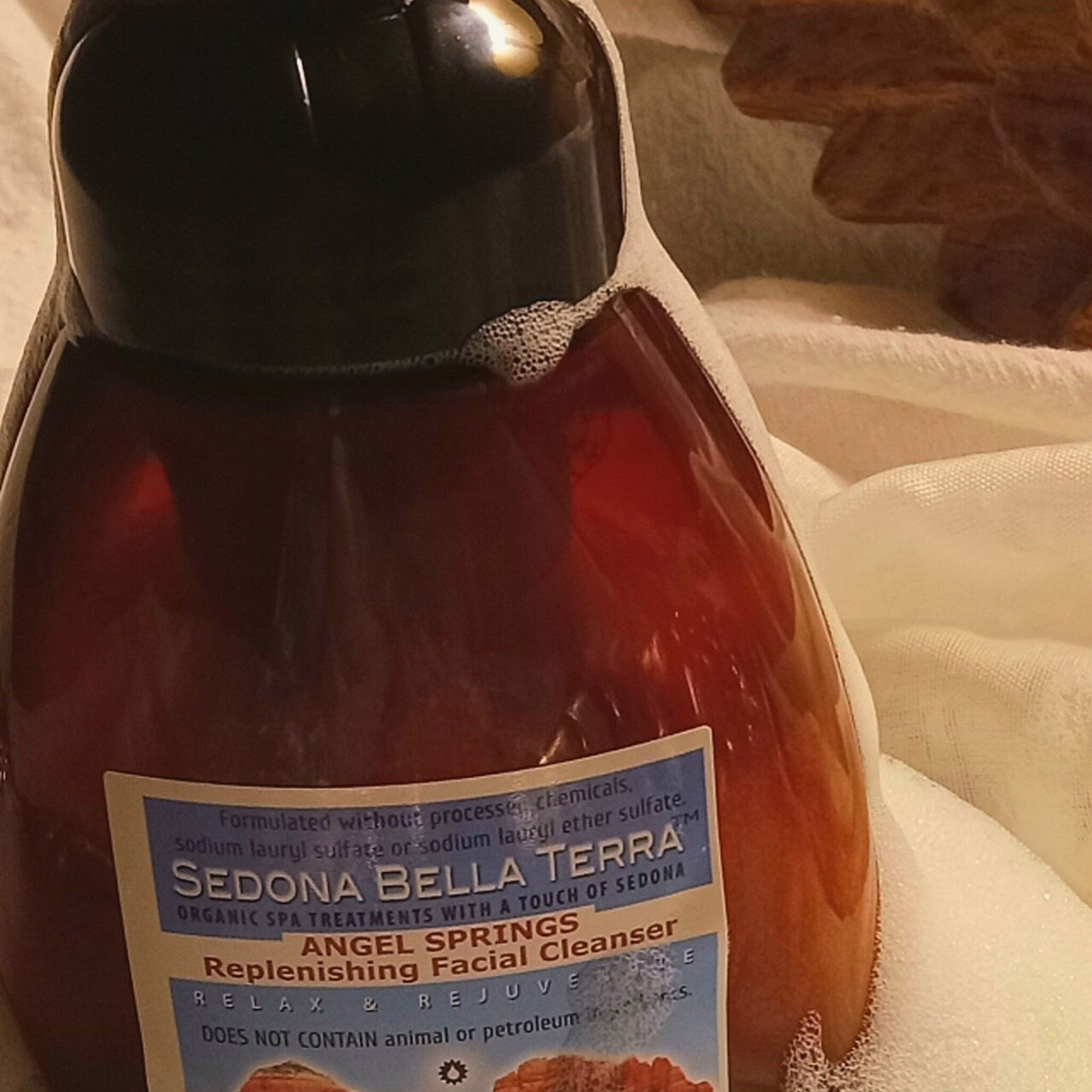 Facial cleanser bottle, brown liquid, black cap, white label, and white foam around it.