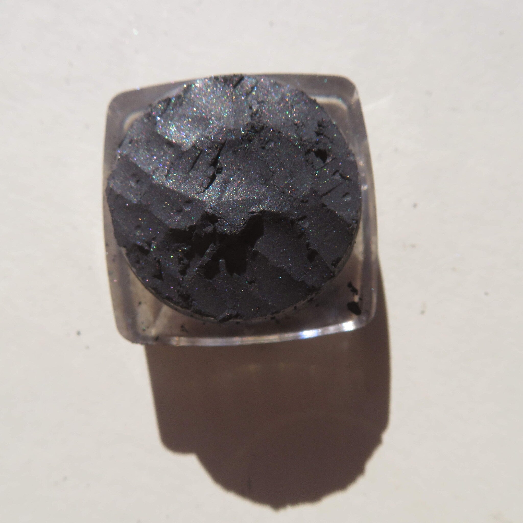 Close-up of black shimmer loose mineral eyeshadow with sparkling silver flecks in a small jar
