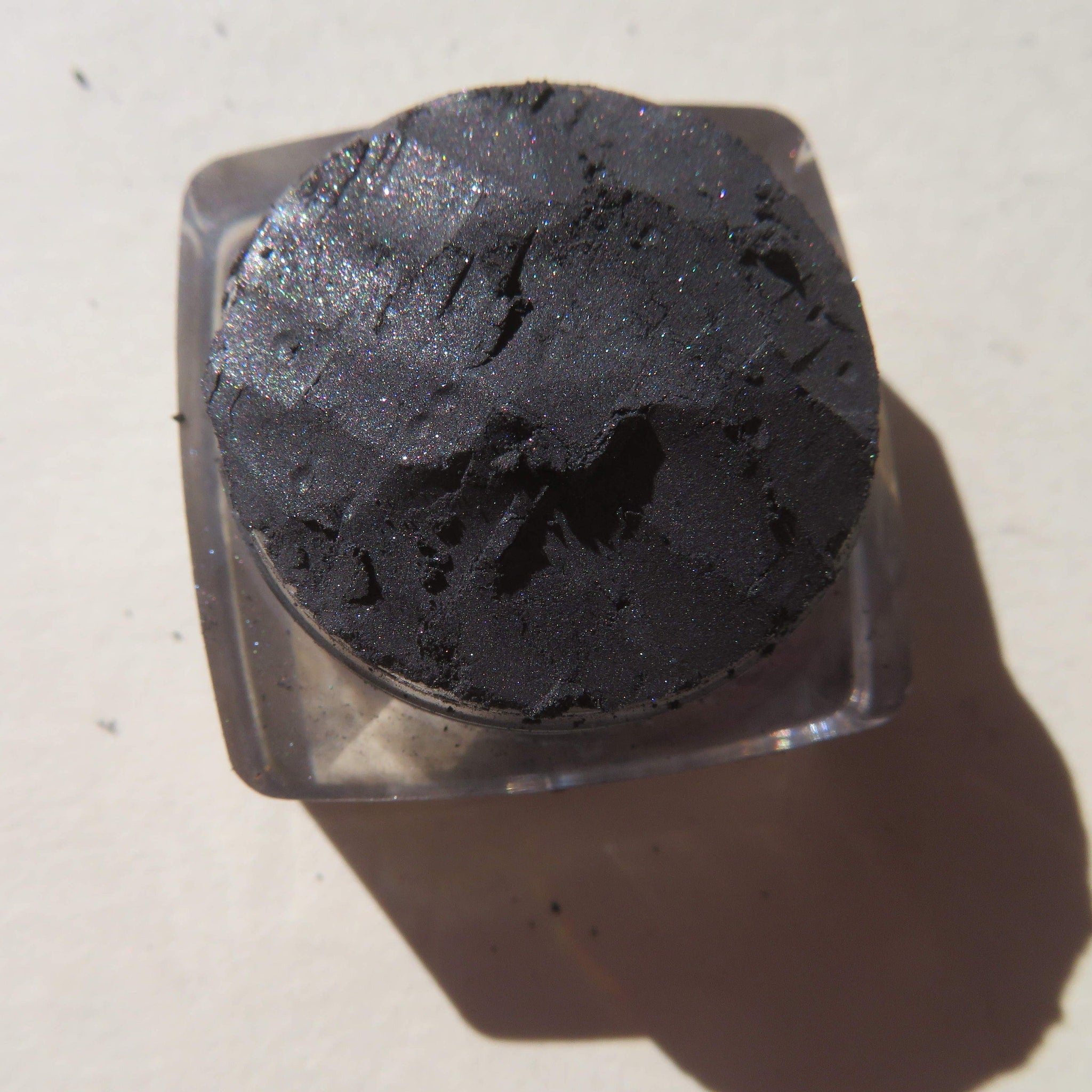 Side view of black shimmer loose mineral eyeshadow with reflective sparkles in a clear jar