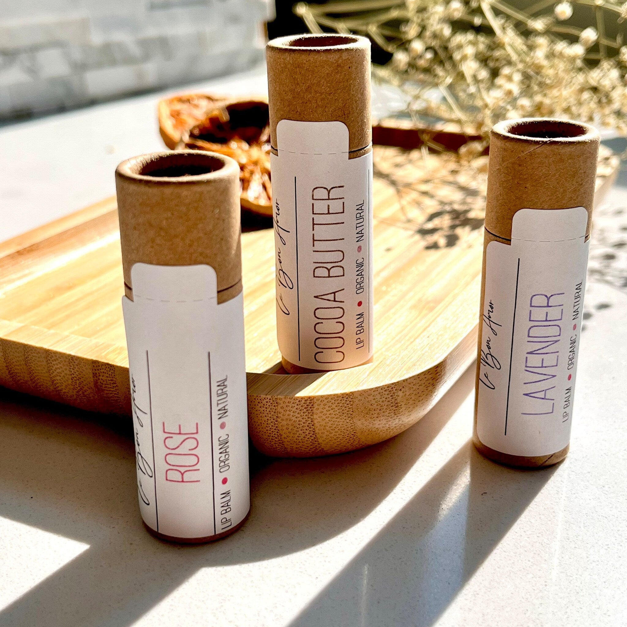 Lip balm tubes in brown cardboard, white labels with text, on a wooden tray with Le Bon Amor brand