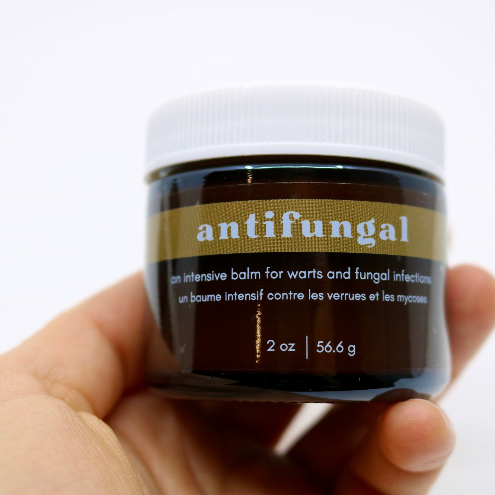 Antifungal balm jar, brown glass container with white lid, held in hand, "antifungal" label visible
