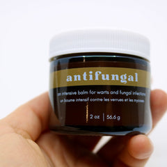 Antifungal balm jar, brown glass container with white lid, held in hand, "antifungal" label visible
