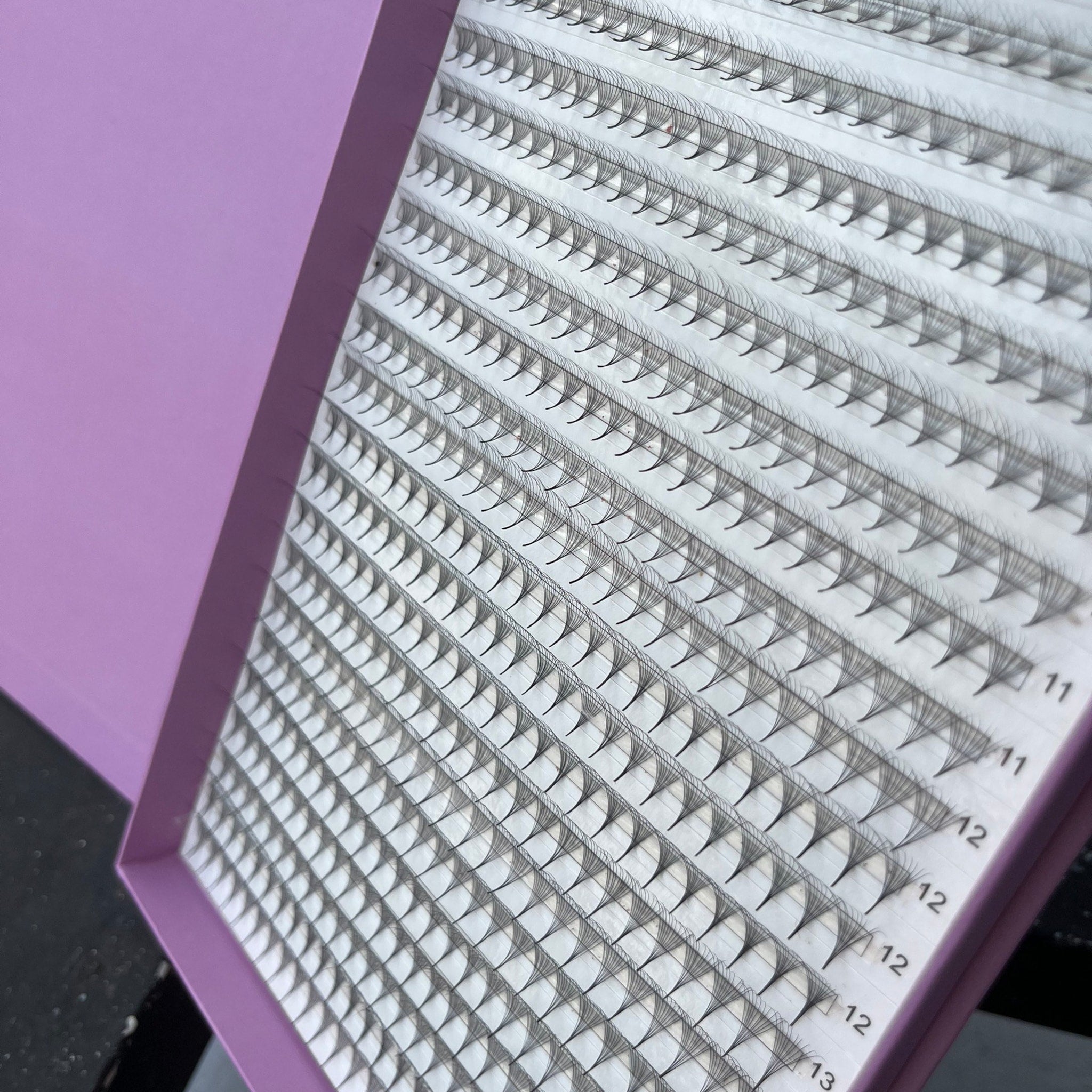 Eyelash extensions in a tray with black synthetic fibers and a purple box with white labels.