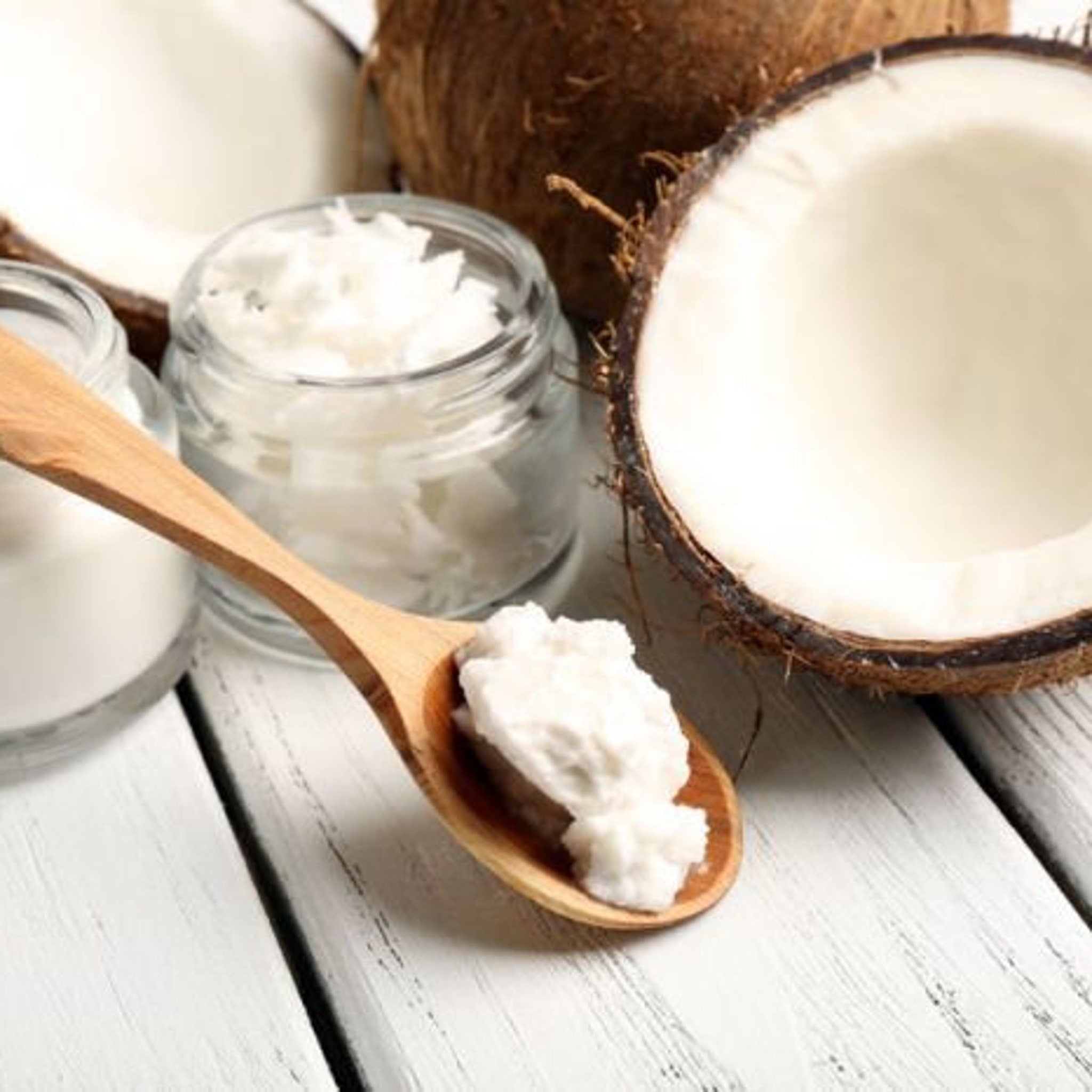 Coconut oil in white and clear jars with wooden spoon on white wood surface