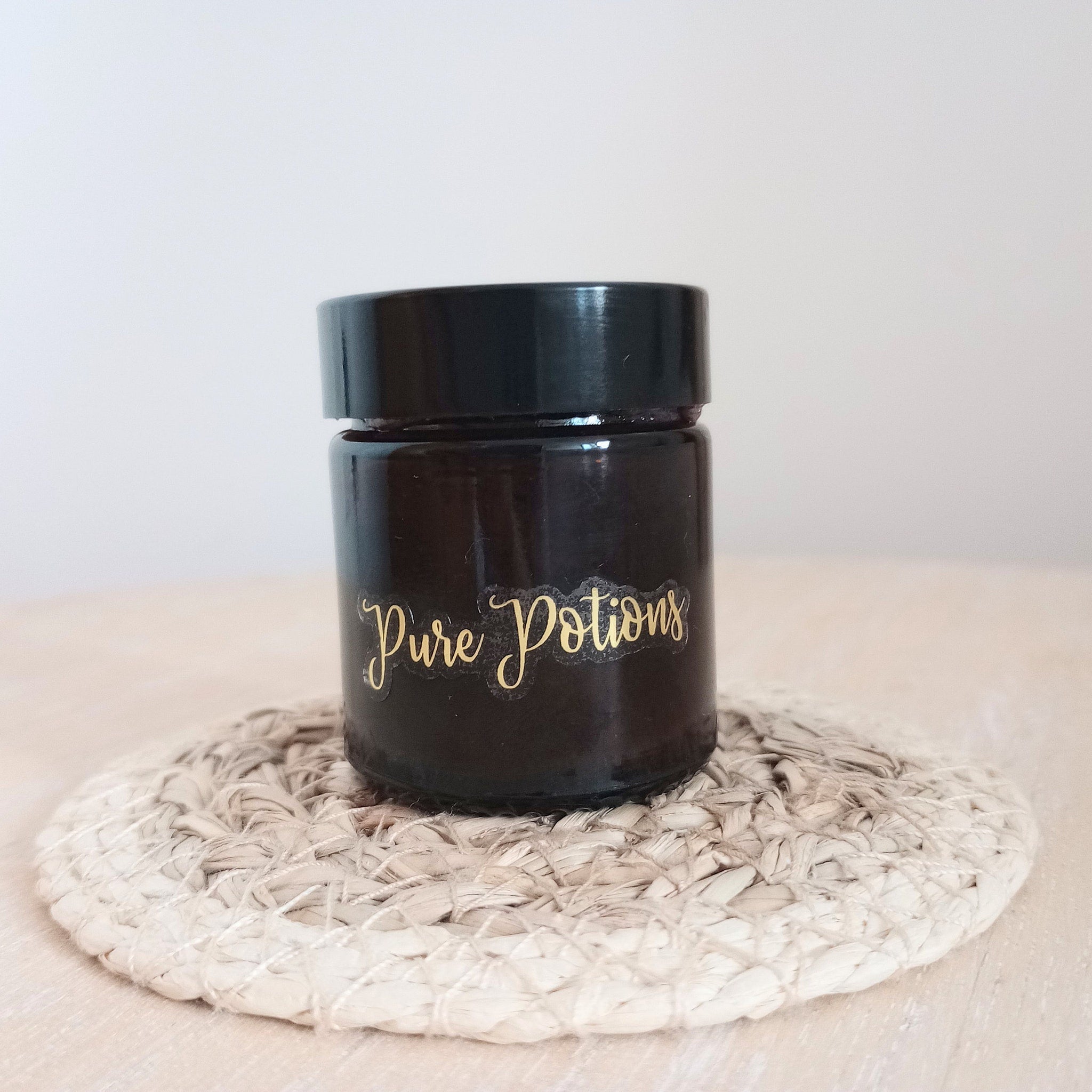 Dark glass jar with gold "Pure Potions" label on woven coaster