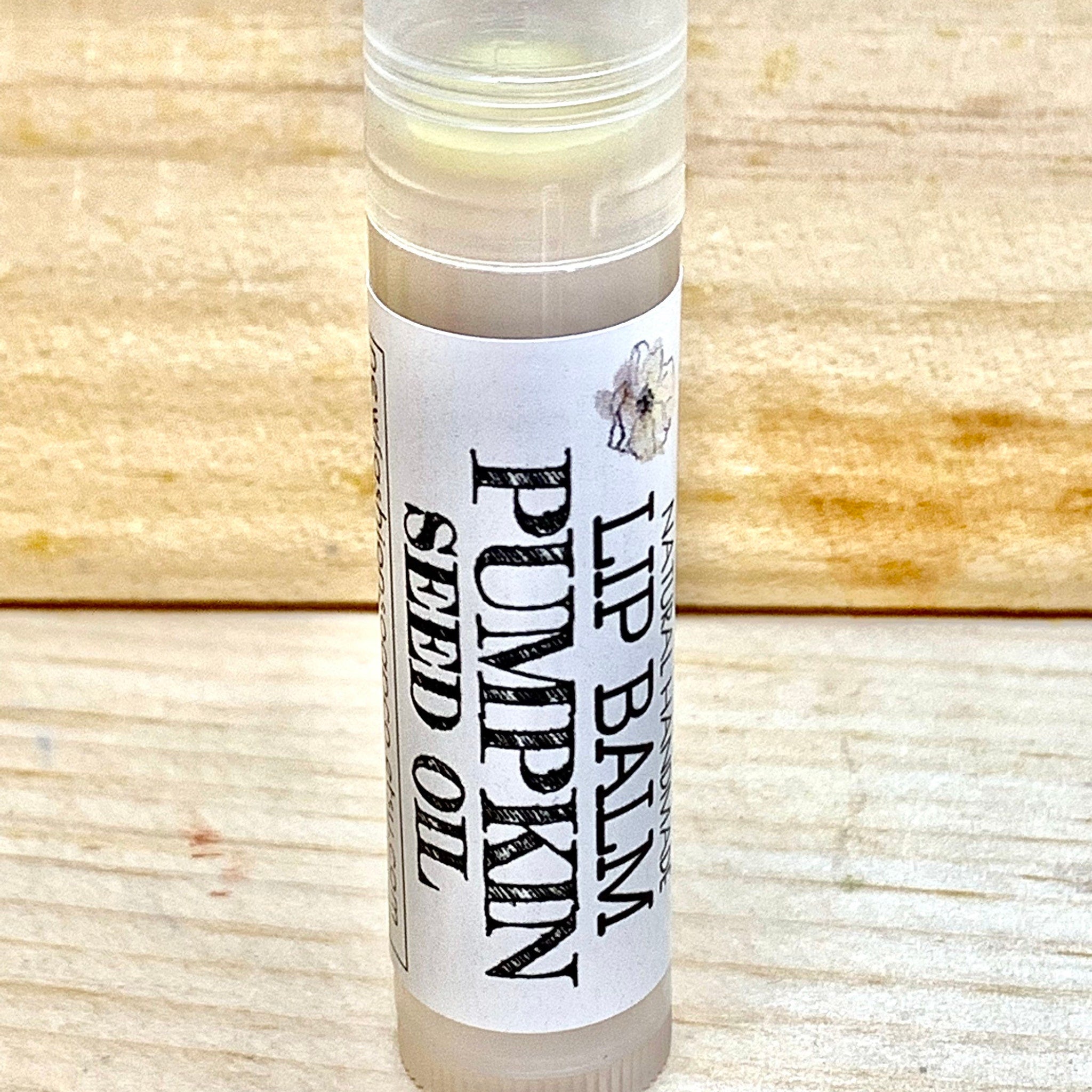 Lip balm tube with white label, black text, and clear plastic cap on wooden background