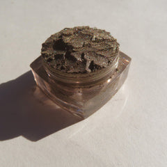 Eyeshadow pot with bronze shimmer, textured surface, and clear glass container