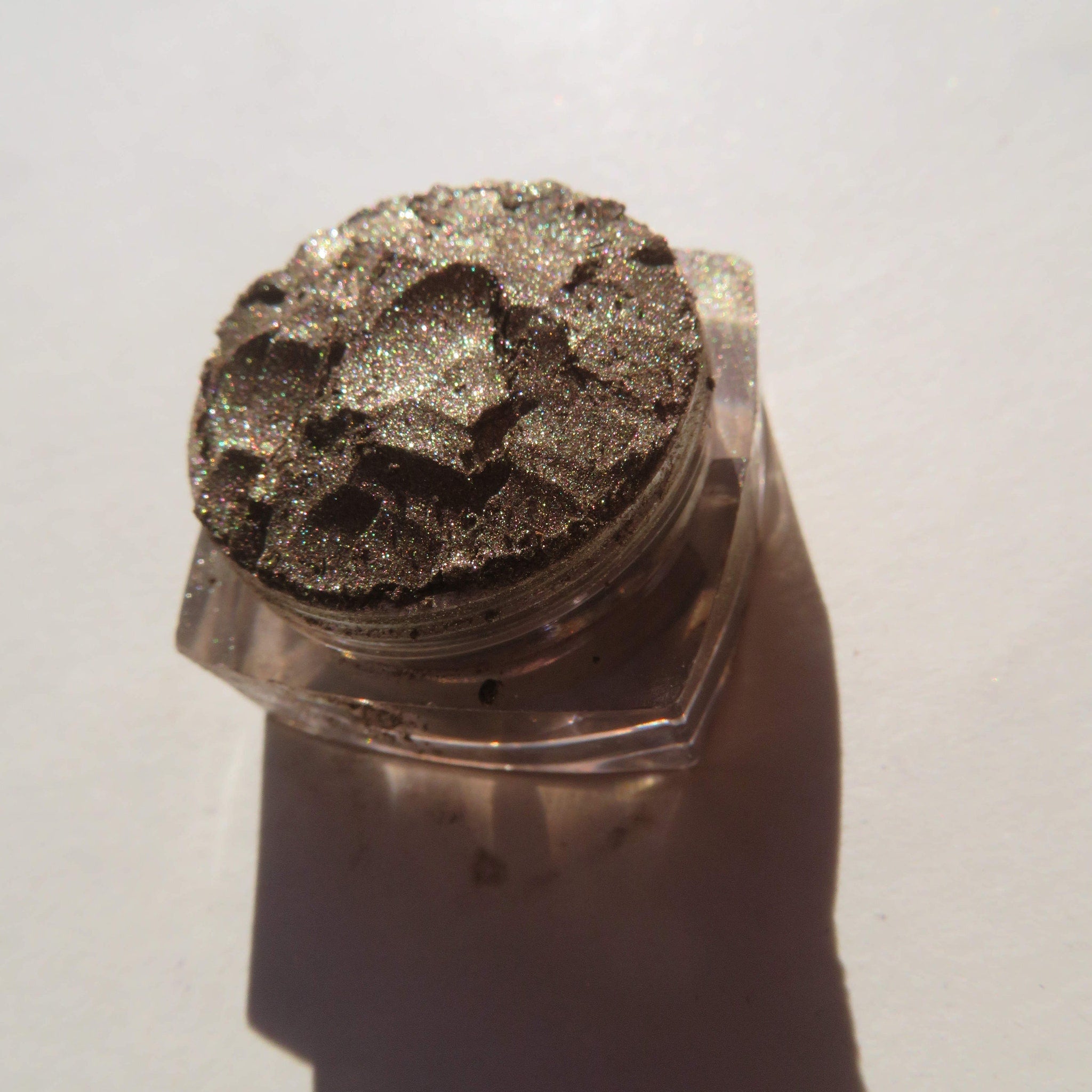 Eyeshadow pot with bronze shimmer, clear plastic container, and shadow on white surface