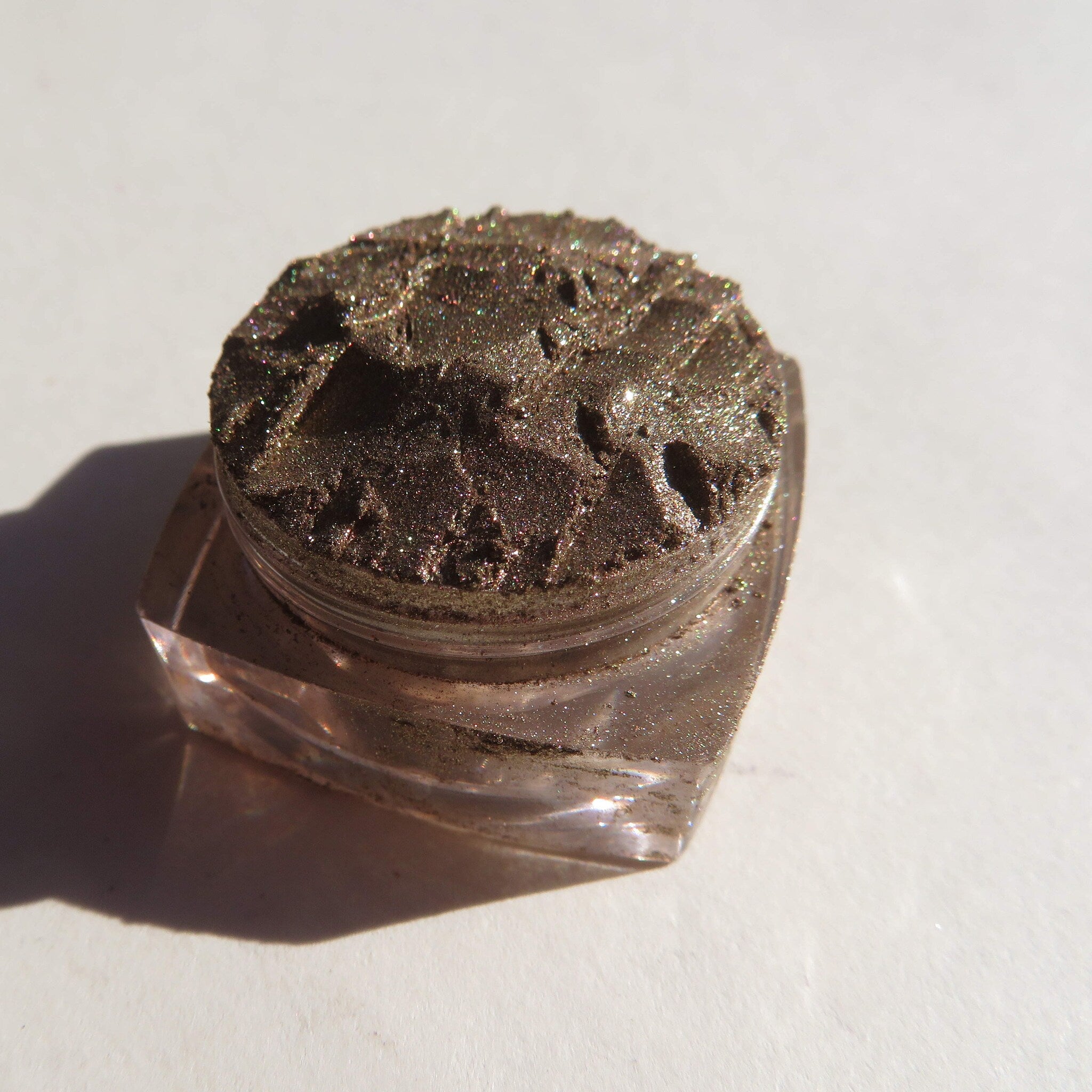 Glitter eyeshadow in bronze color with textured surface in a clear jar