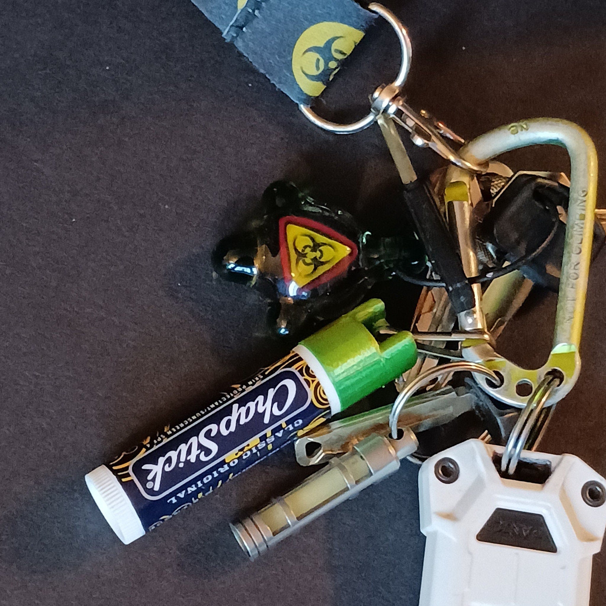Keychains with ChapStick, green cap, silver rings, and white case on dark surface