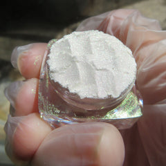 Close-up of loose mineral eyeshadow with white shimmer and green gold sheen in vegan powder form