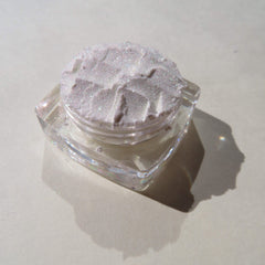 Side angle view of loose mineral eyeshadow in white shimmer with green-gold sheen, showcasing fine pigment texture