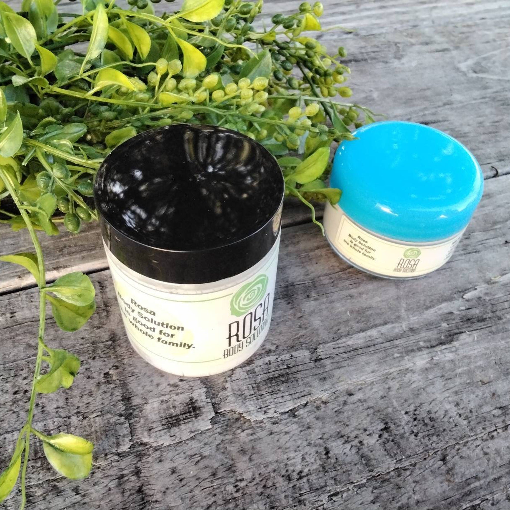 Body solution jars with black and blue lids, ROSA brand label, on wood surface