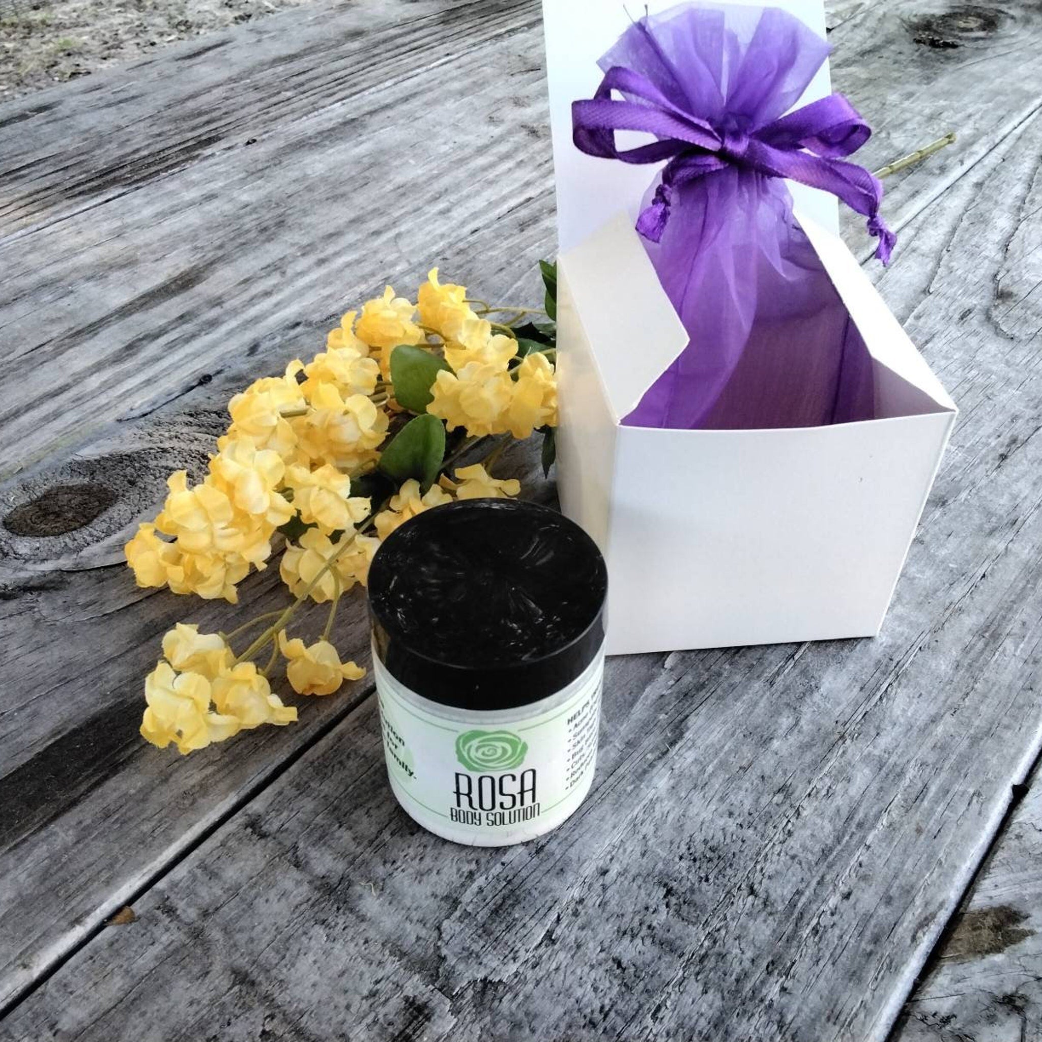 Body solution jar with black lid, white label, and yellow flowers on wooden surface