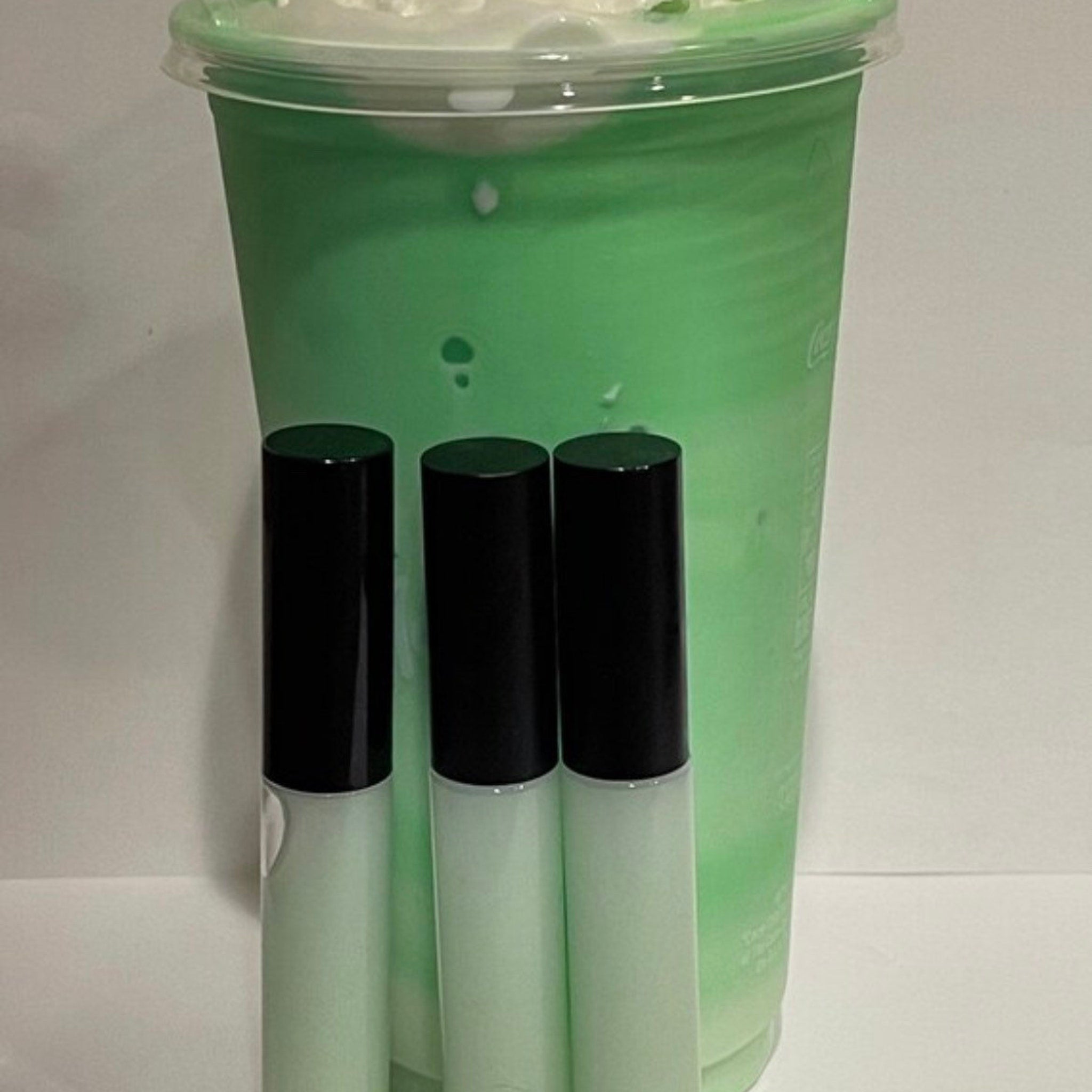 Green drink and lip gloss set, green beverage in clear plastic cup, black lip gloss tubes