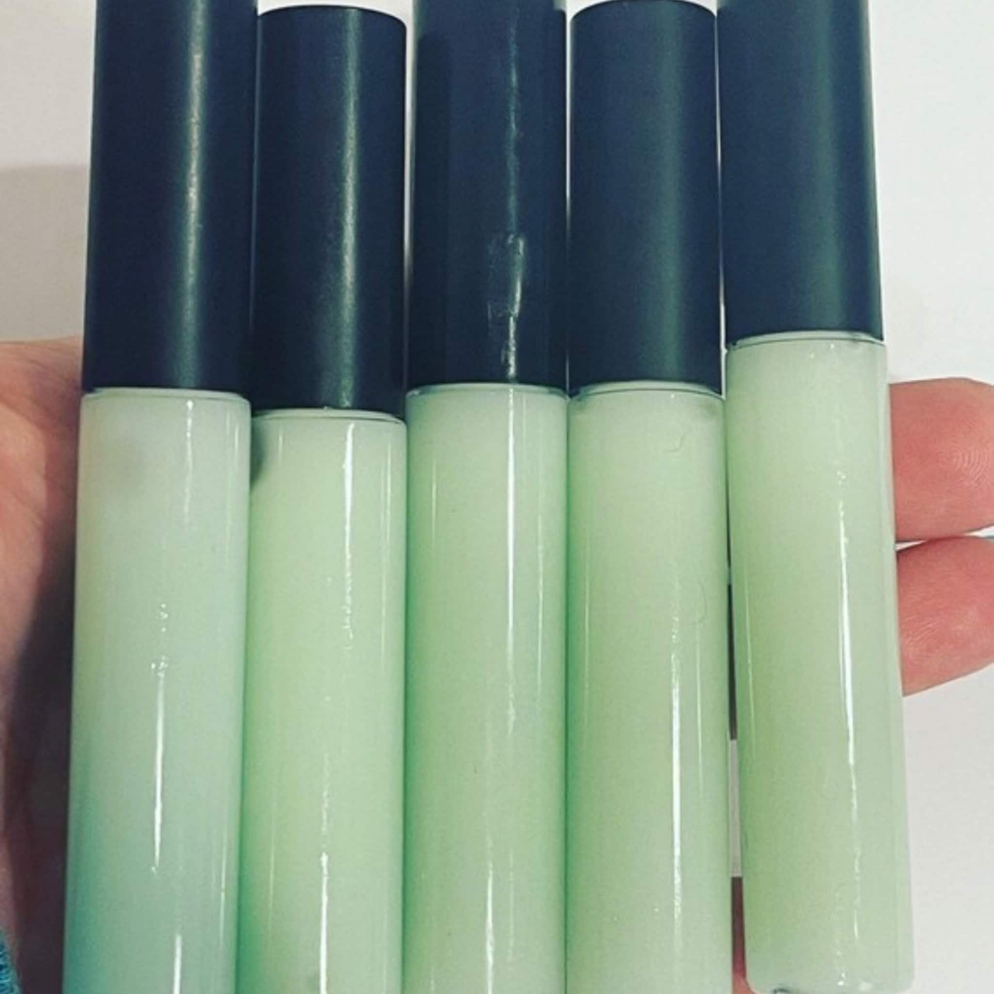 Lip gloss tubes with black caps and pale green liquid, held in hand