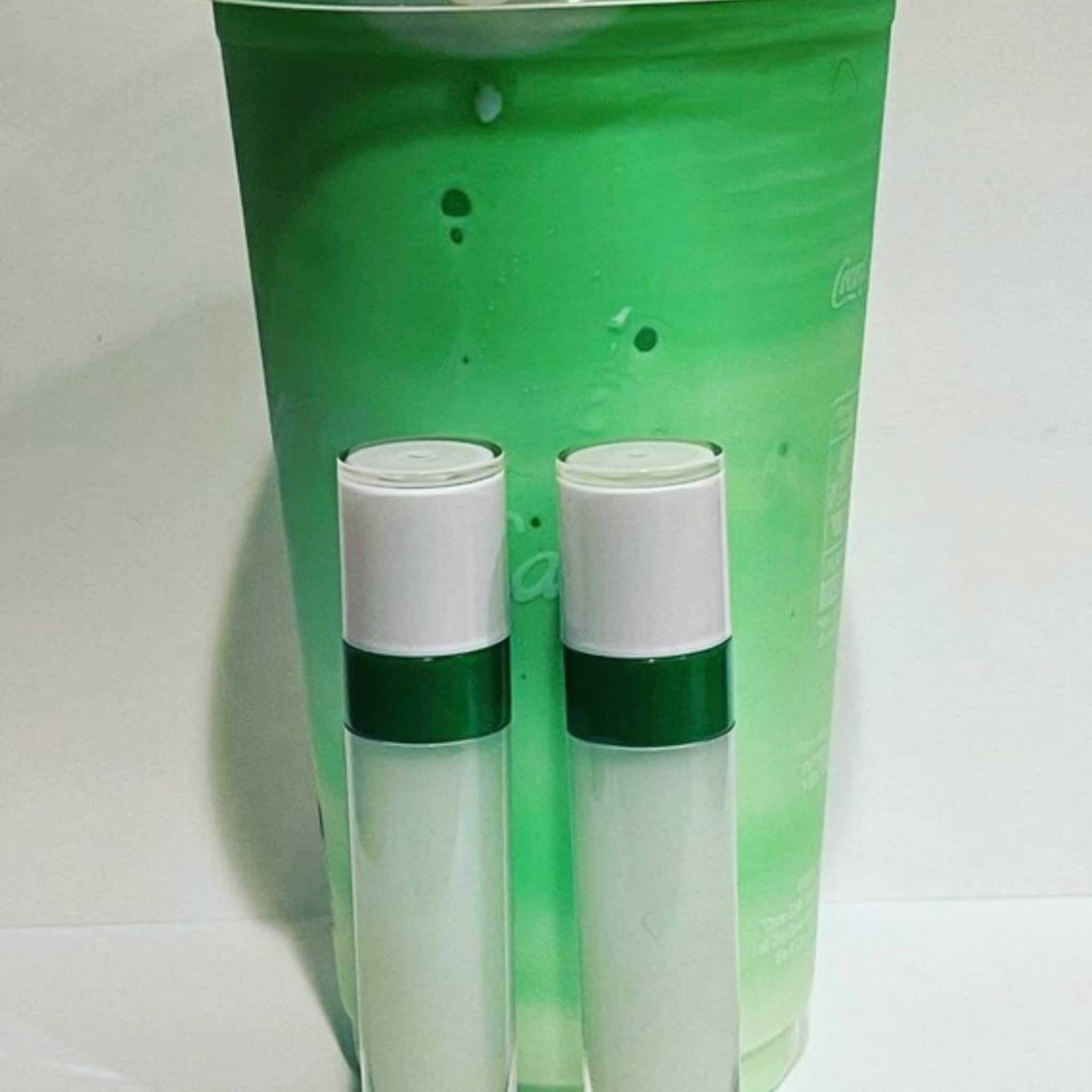 Lip gloss bottles with white, green and clear glass, next to green drink in a Coca-Cola cup