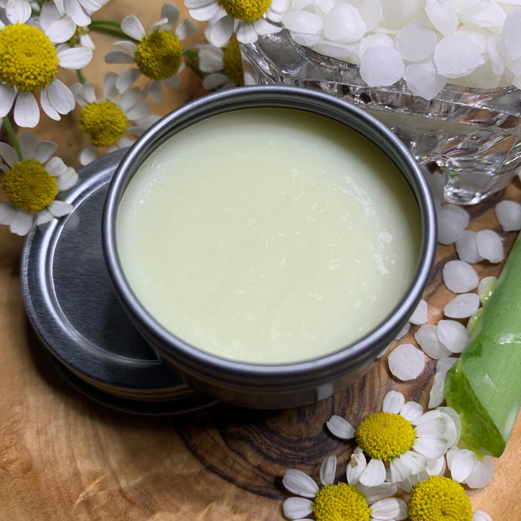 Balm in metal tin, light green color, with open lid on wooden surface