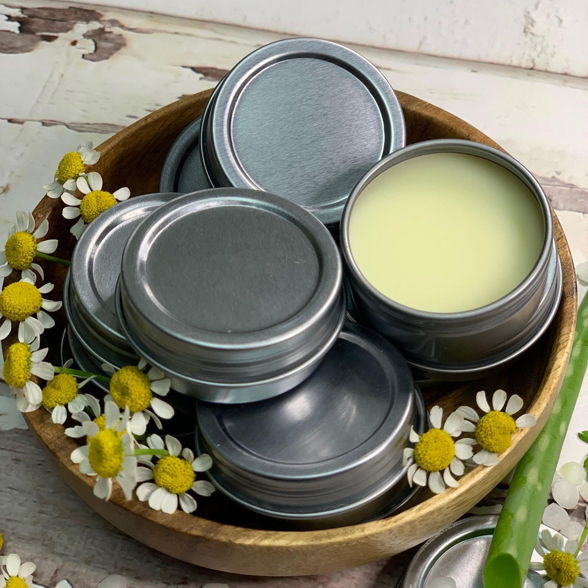 Metal tins with silver lids, yellow balm, and wooden bowl with flowers
