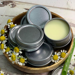 Metal tins with silver lids, yellow balm, and wooden bowl with flowers