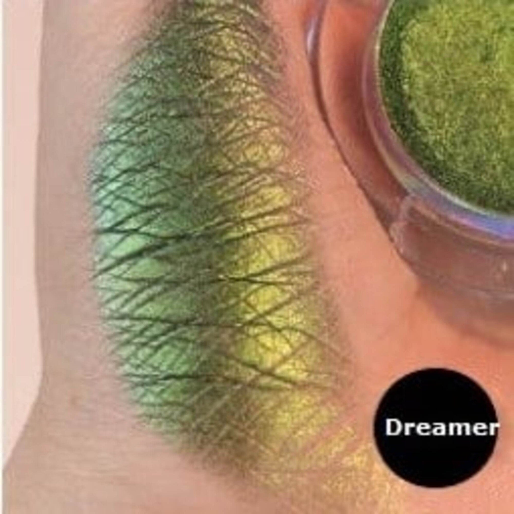 Eyeshadow swatch with green and yellow shimmer, Dreamer brand label visible, applied on skin