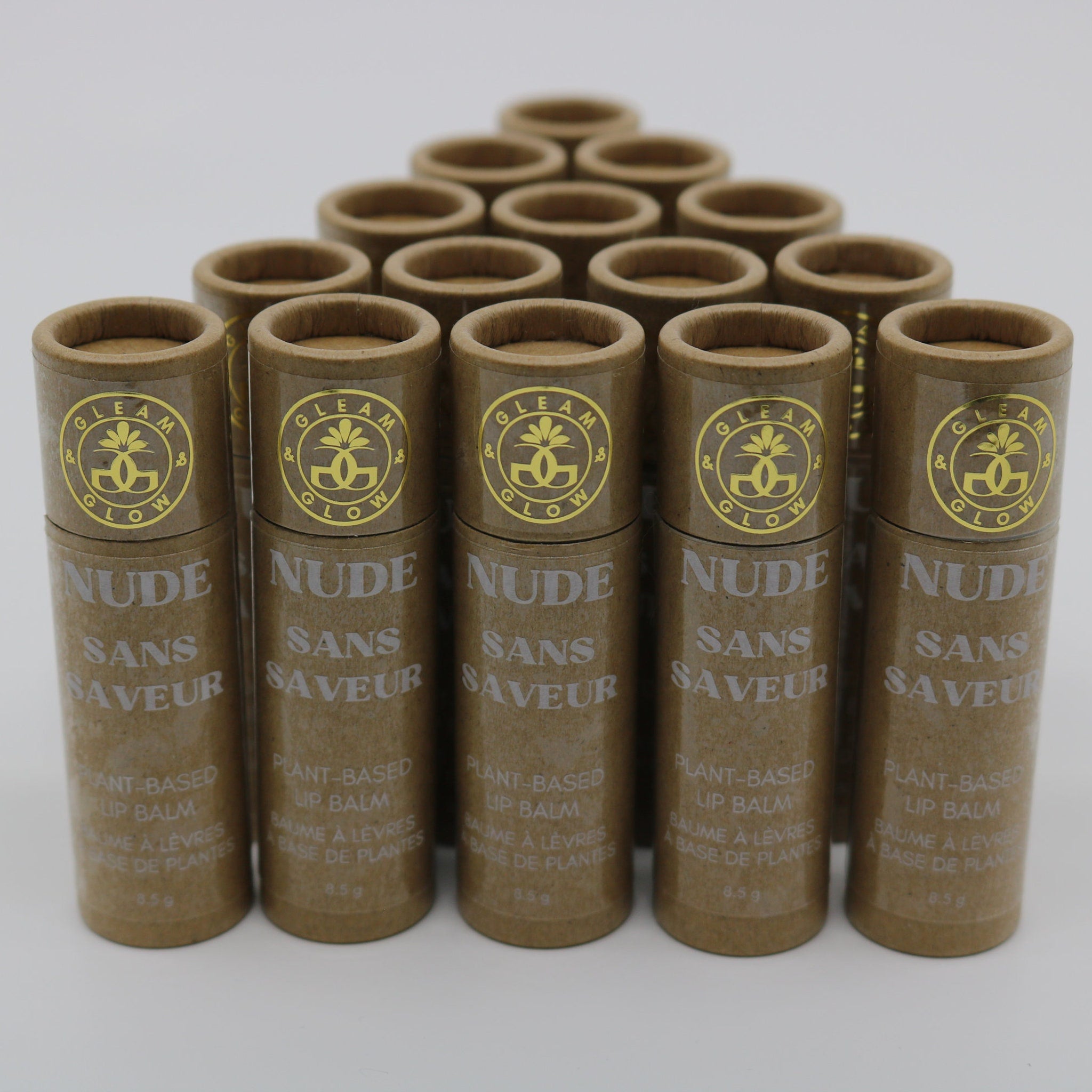 Lip balm tubes in brown cardboard with gold logo and "NUDE" text, arranged in a pyramid
