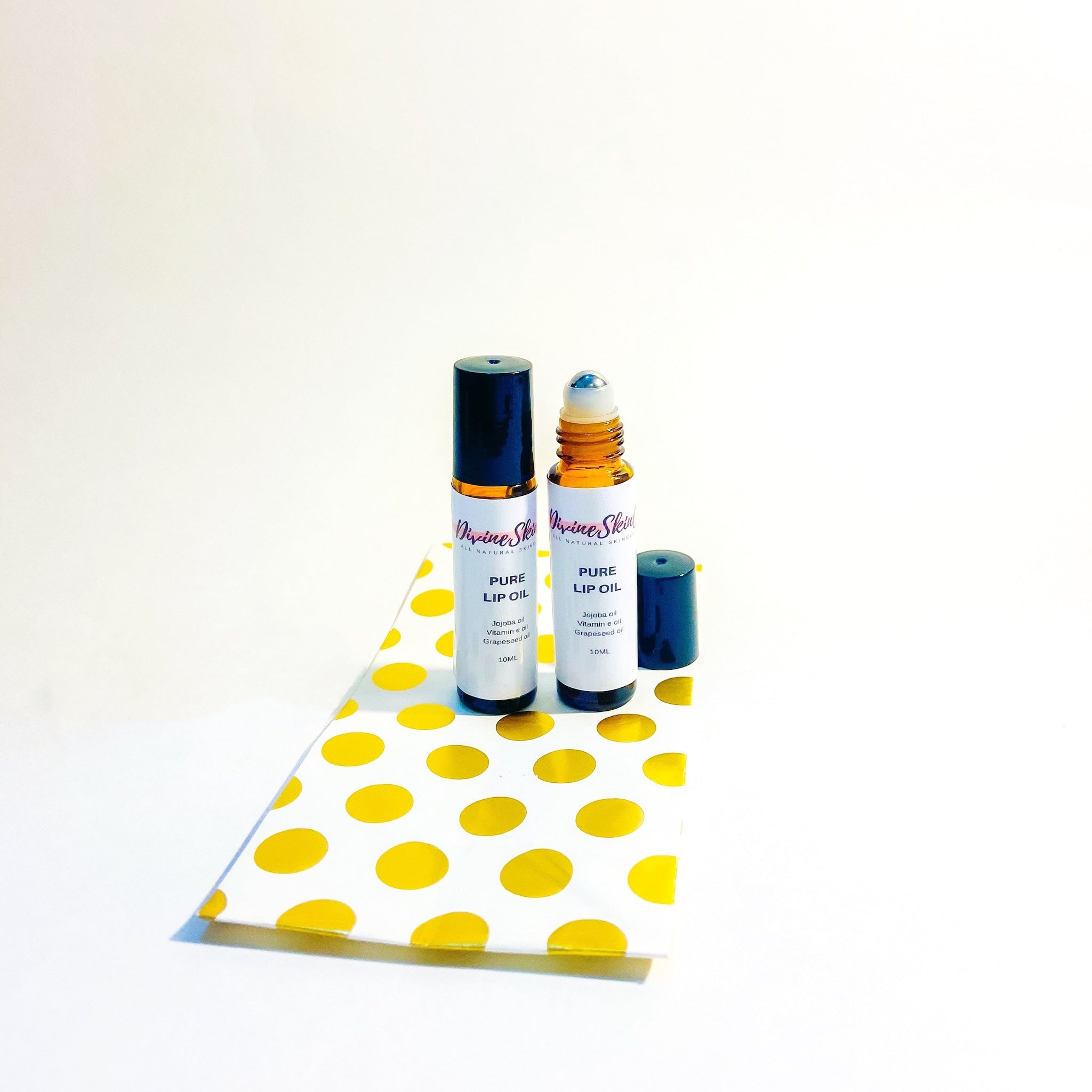 Lip oil bottles with black and brown caps, white labels, and Divine Skin branding, on a polka dot paper