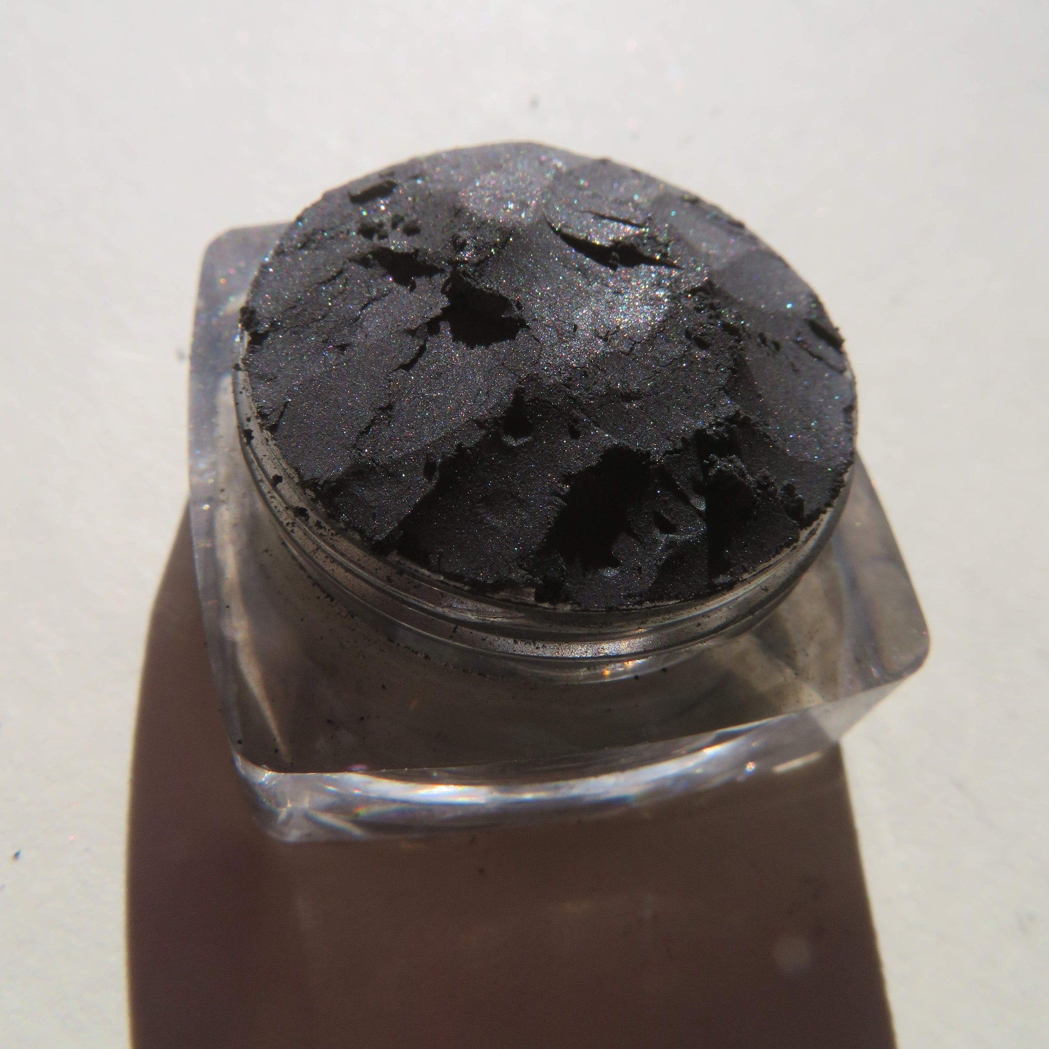 Close-up of black shimmer loose mineral eyeshadow with sparkling silver flecks in a sleek jar