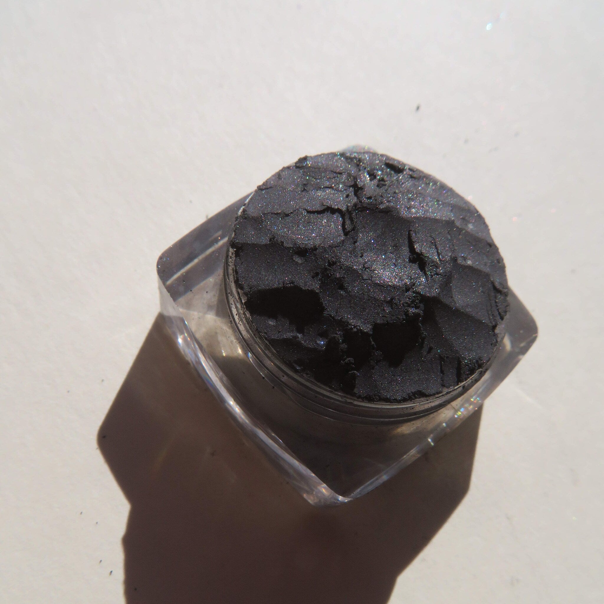 Hand applying black shimmer mineral eyeshadow with brush, creating a smoky eye look