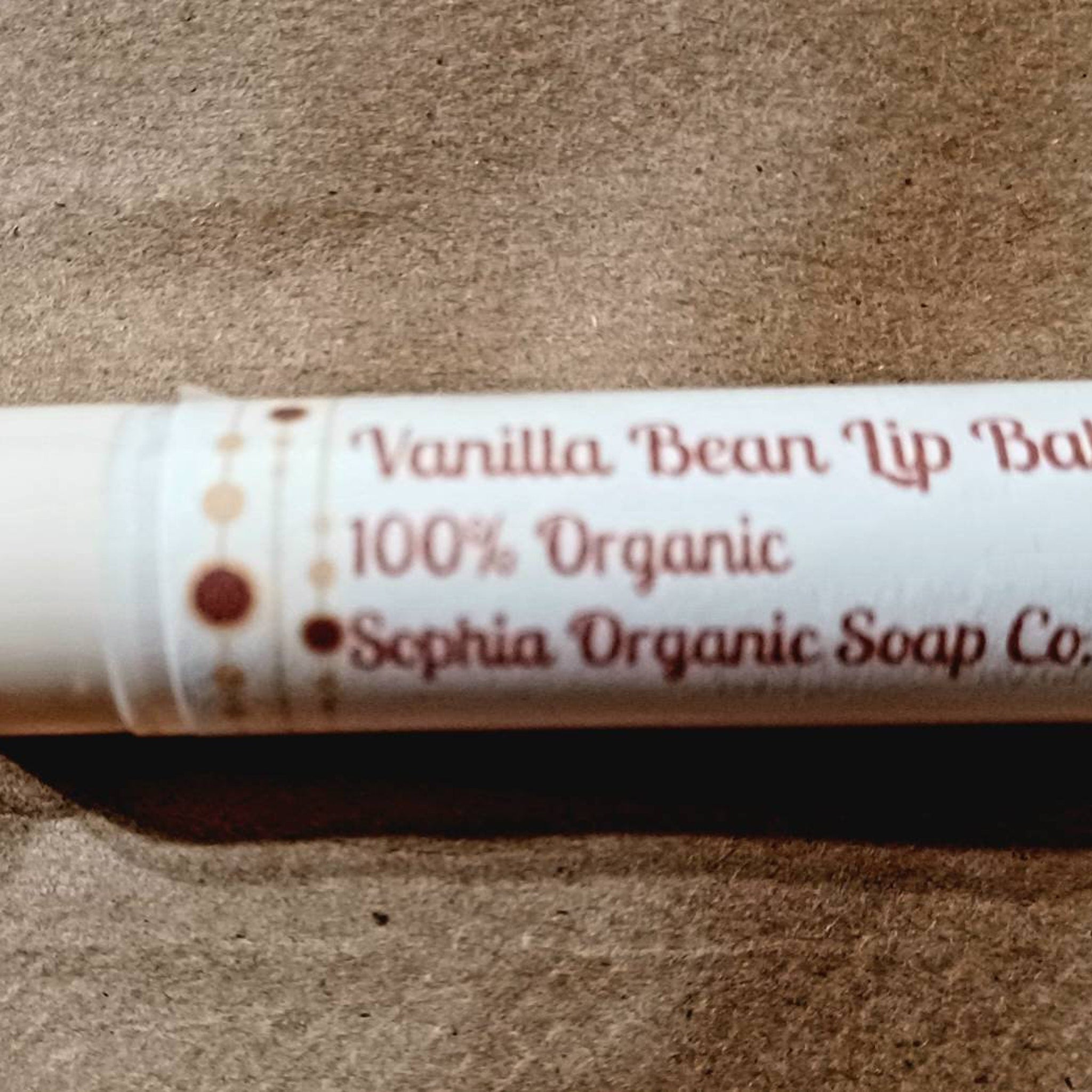 Lip balm tube with white label, brown text, and Sophia Organic Soap Co. branding on brown surface