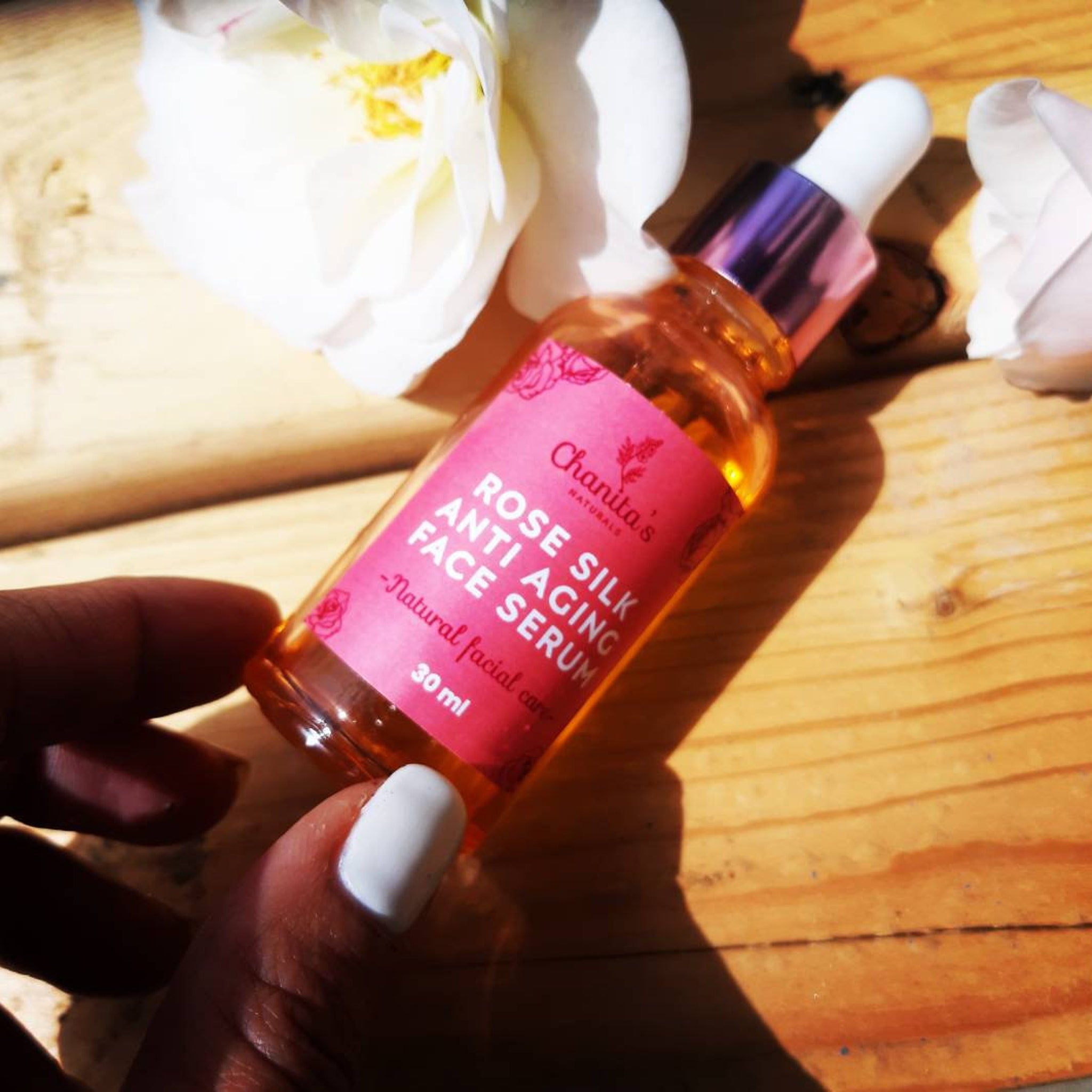 Face serum bottle with pink label, clear liquid, and white dropper top, held by hand