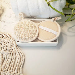 Facial cleansing pads, beige and white round pads, with loop and strap detail, in a dish