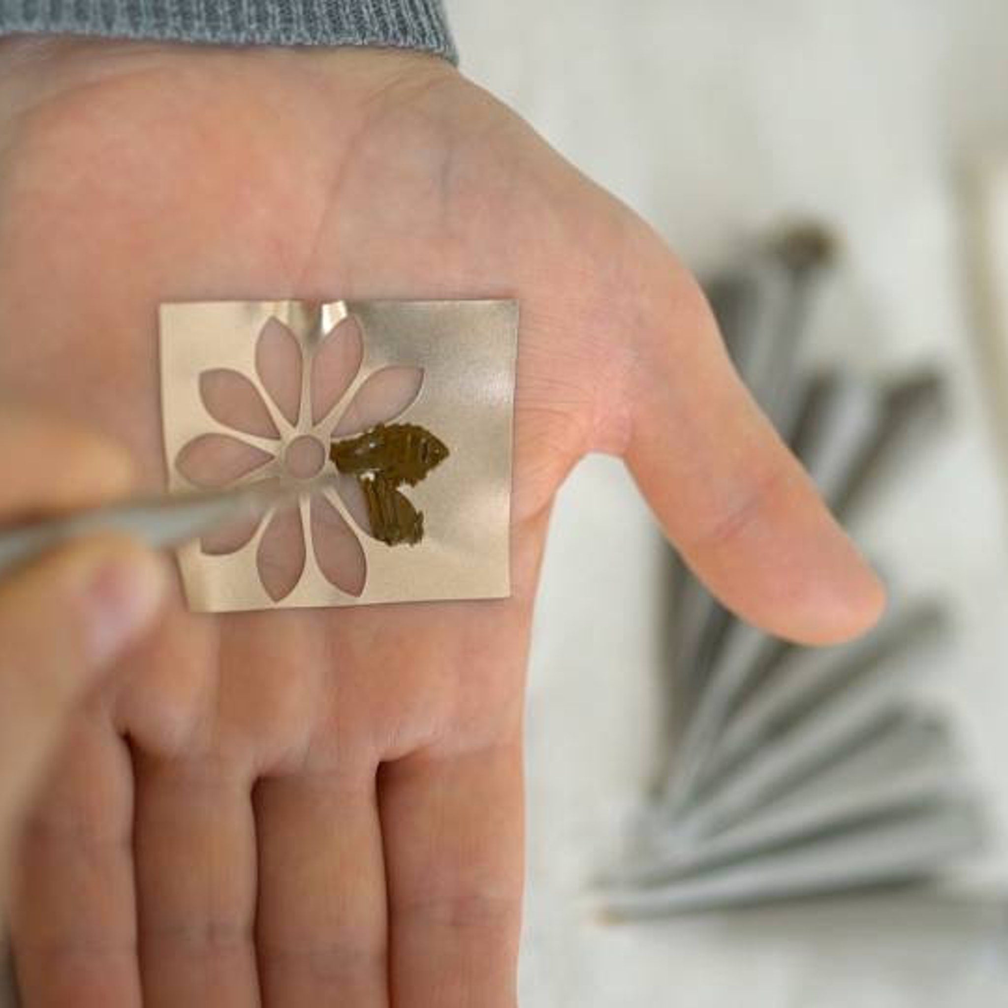 Metal stencil with flower pattern, held in hand with tool, for application