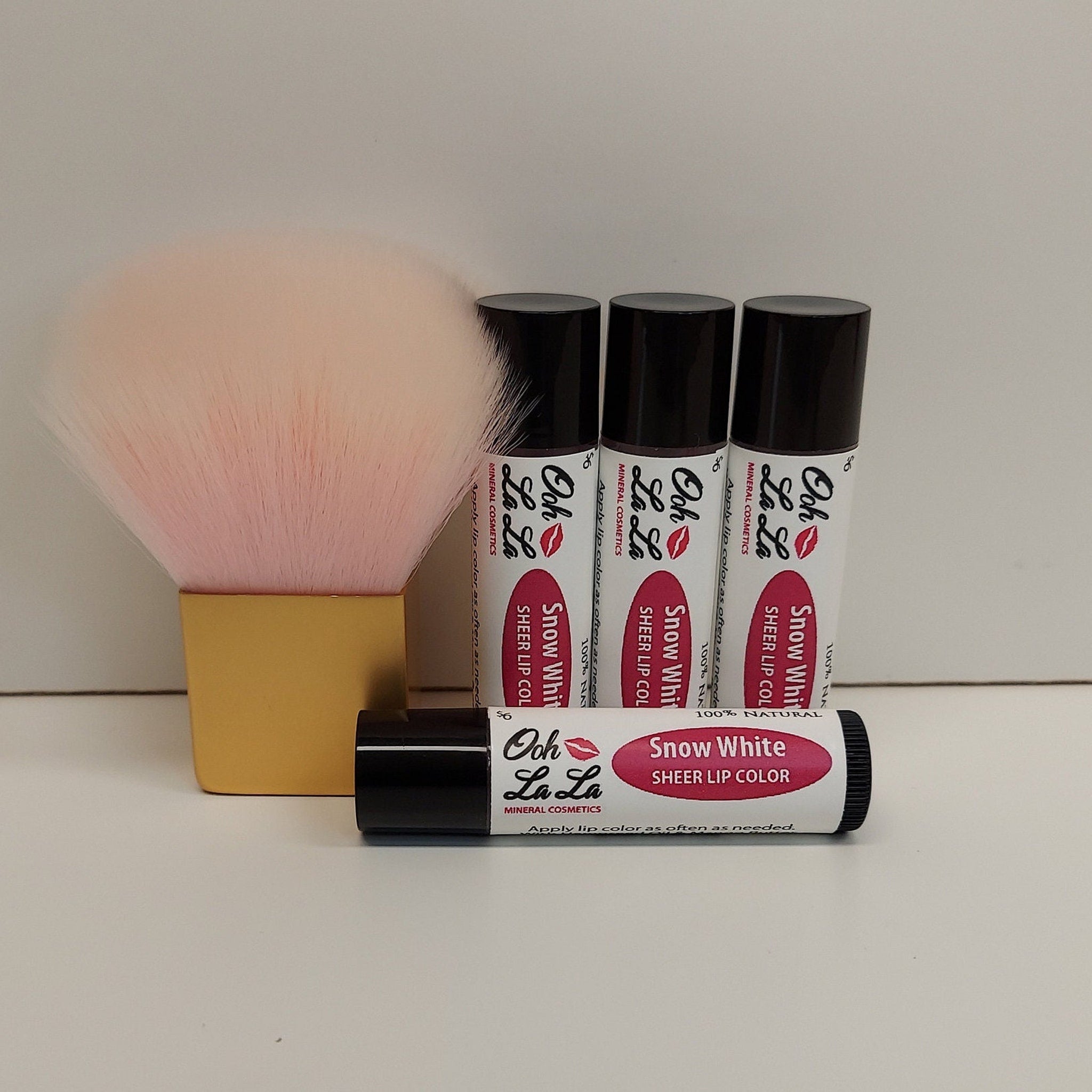 Sheer lip color tubes with black caps, "Ooh La La" brand, and pink lip brush in gold base