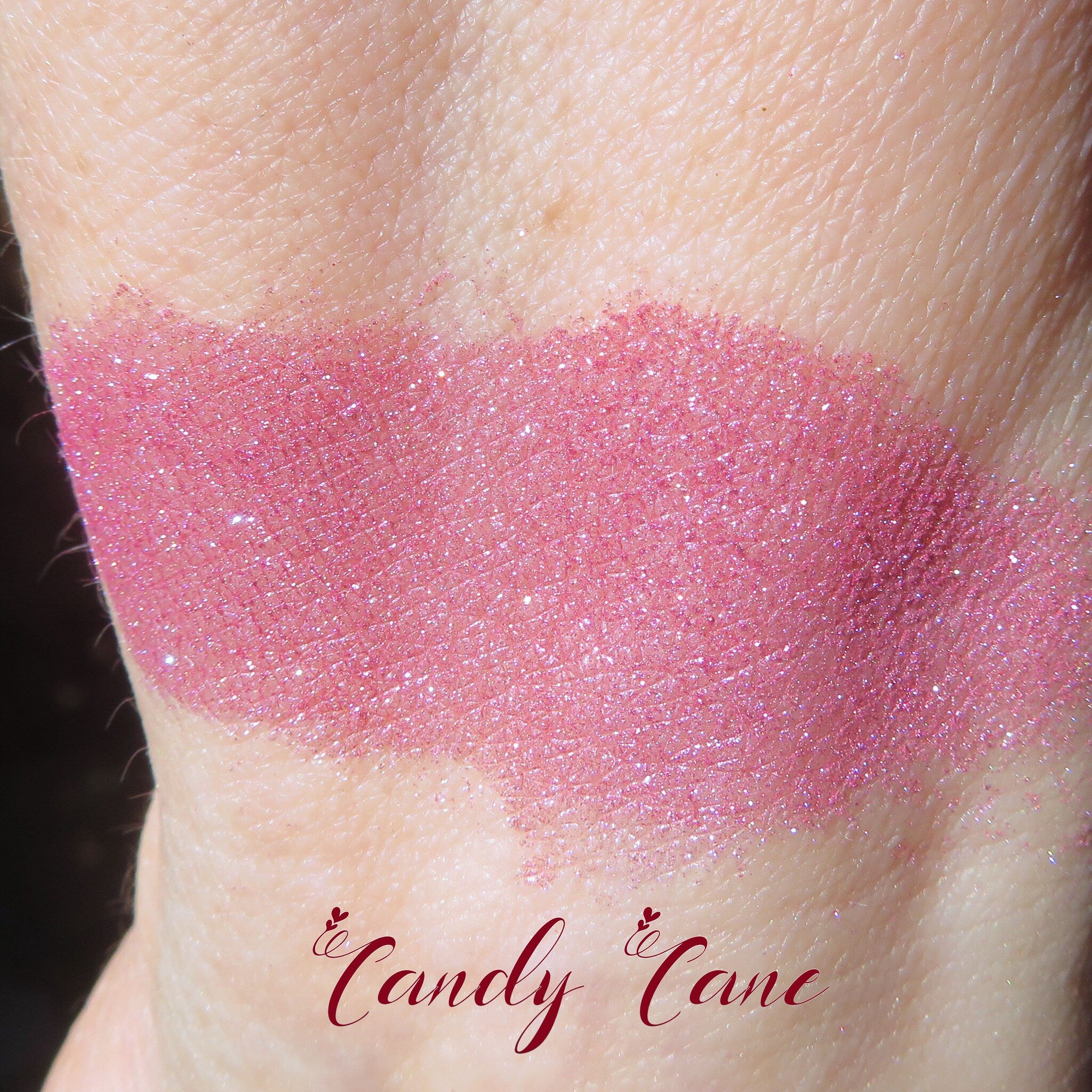 Side view of loose shimmery red-pink vegan mineral eye shadow powder spilling from container