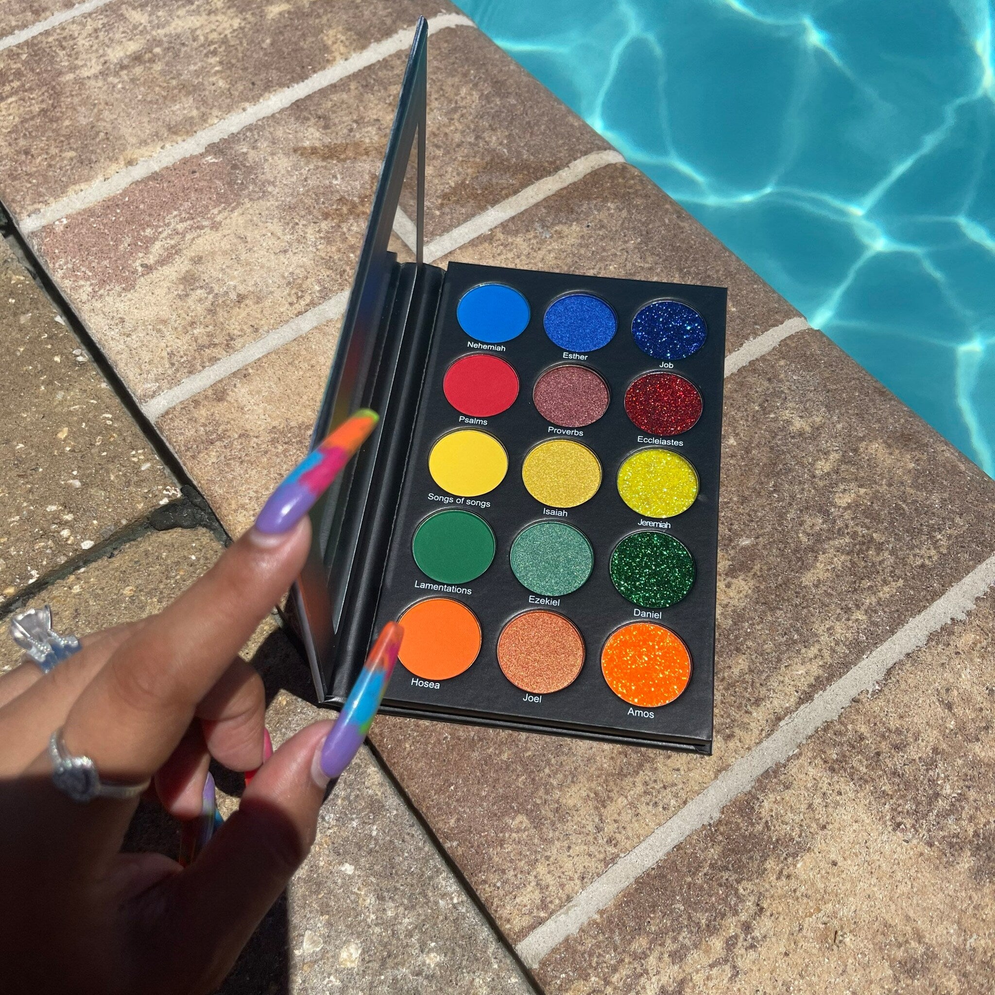 Eyeshadow palette with colorful eyeshadows, black case, held by hand near pool