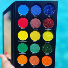 Eyeshadow palette with various colors and textures, held in hand against a blue background