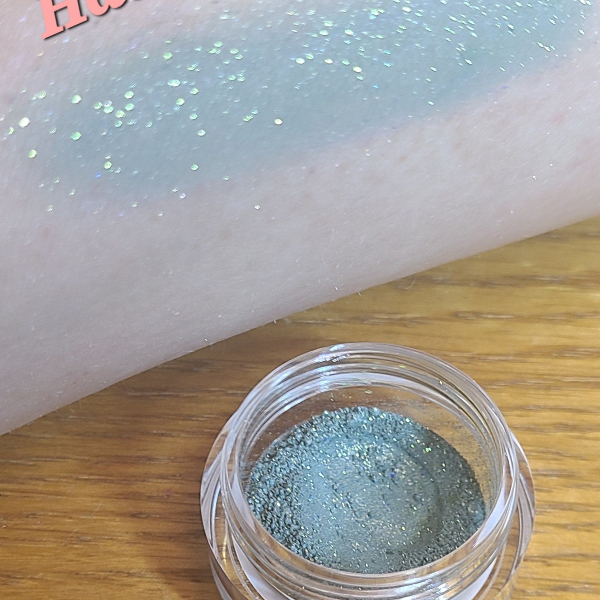Side view of loose blue eyeshadow powder in a transparent sifter jar, showcasing its fine texture and vibrant azure hue