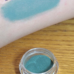 Close-up of vibrant blue loose powder eyeshadow with shimmering flecks in a minimalist jar