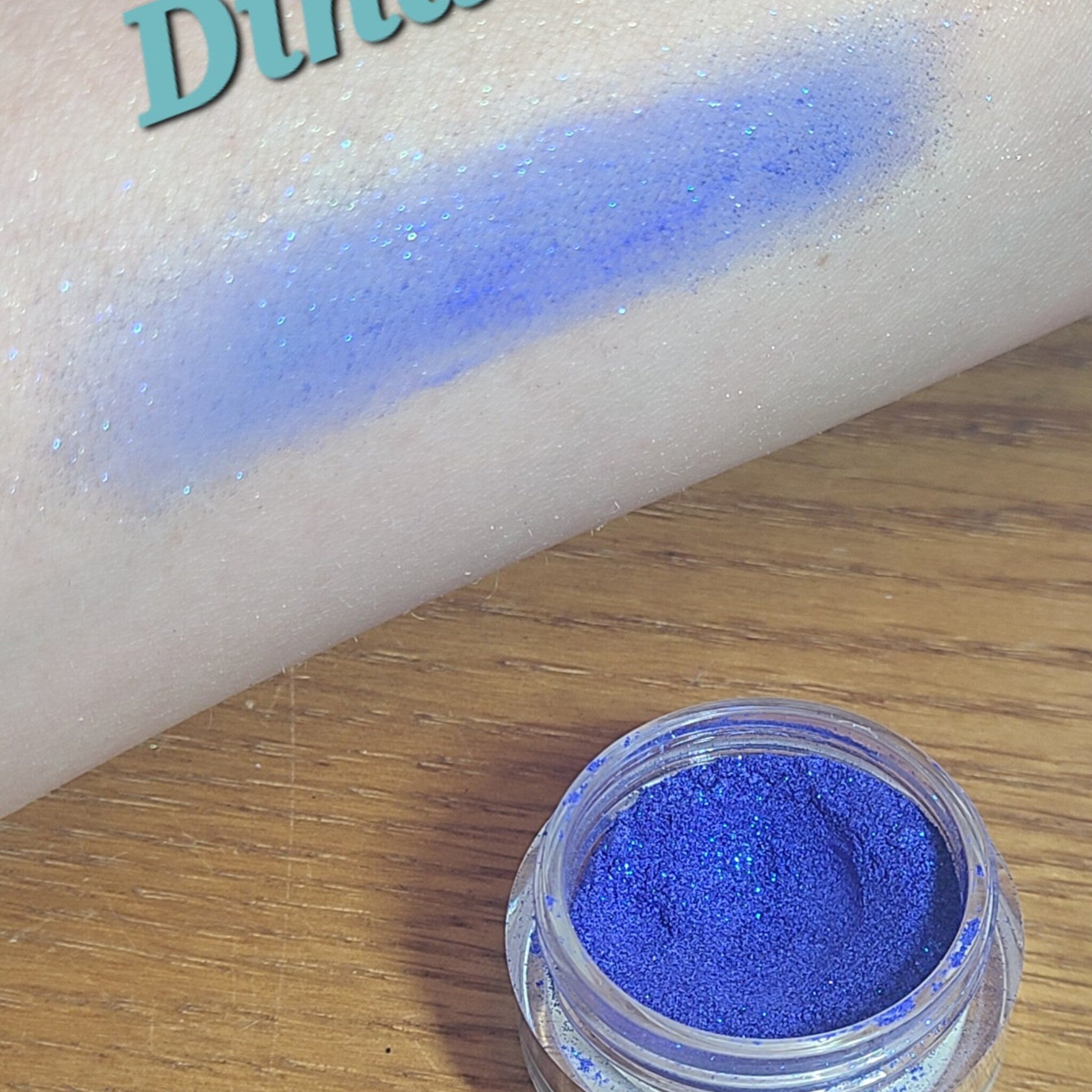 Blue loose powder eyeshadow in a clear glass jar with black screw-top lid and silver label