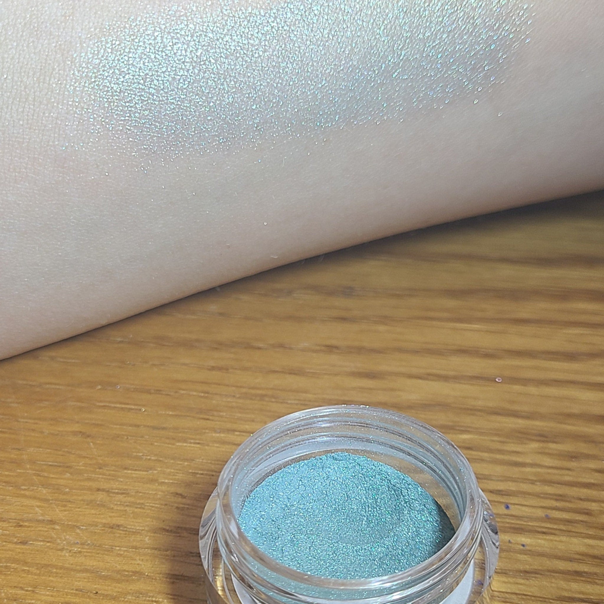 Close-up of vibrant blue loose powder eyeshadow with shimmer particles in a sleek glass jar