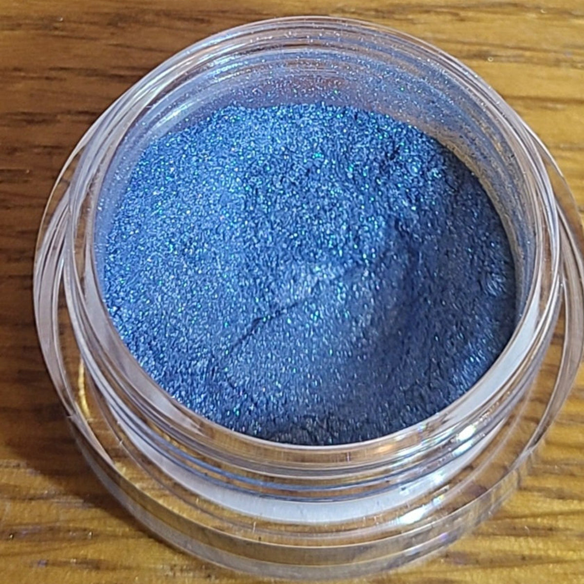 Close-up of loose powder eyeshadow in a vibrant natural blue shade with shimmer particles, displayed in a small round jar.