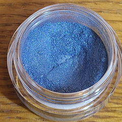 Close-up of loose powder eyeshadow in a vibrant natural blue shade with shimmer particles, displayed in a small round jar.