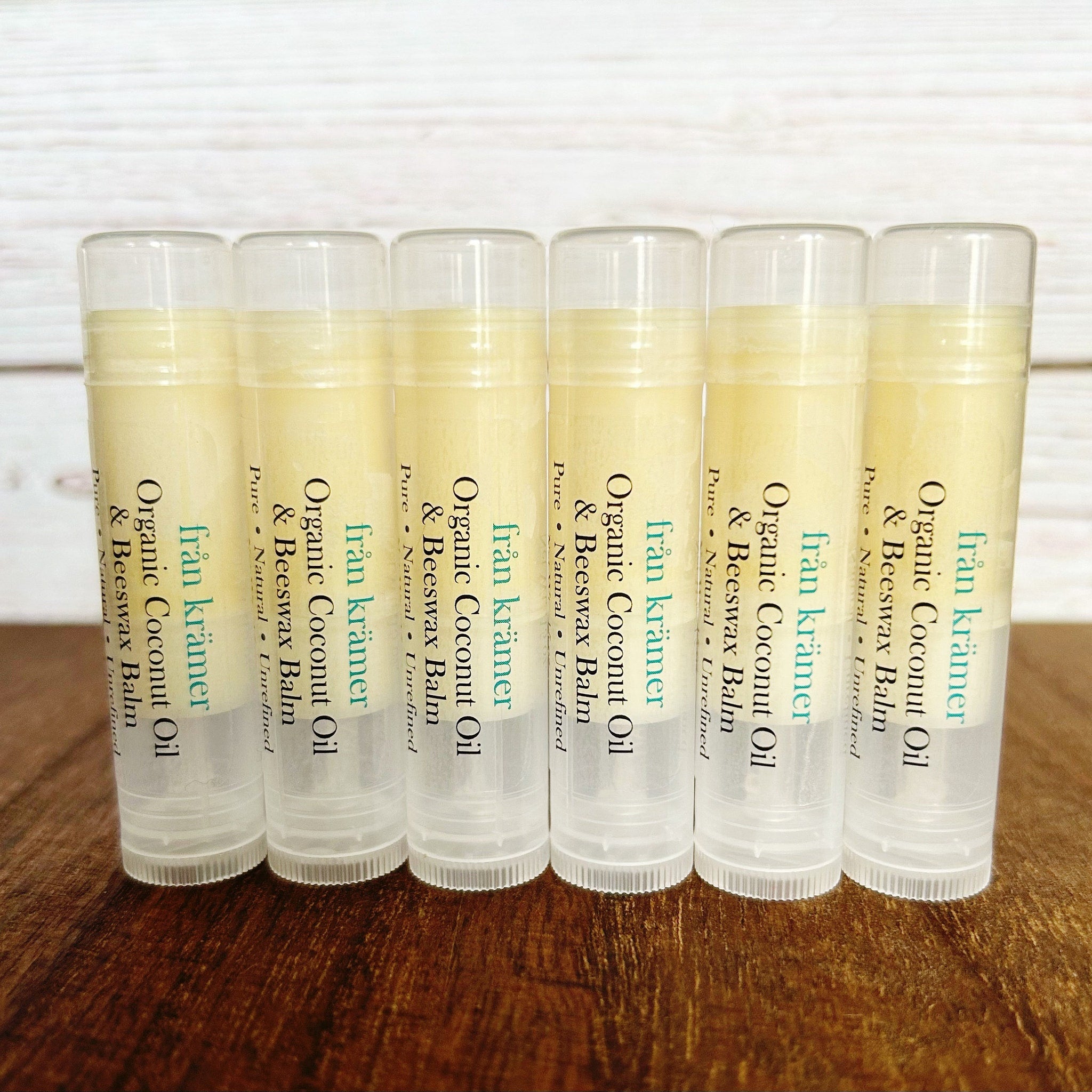 Lip balm tubes with yellow balm, clear plastic, and "från krämer" text labels on a wood surface