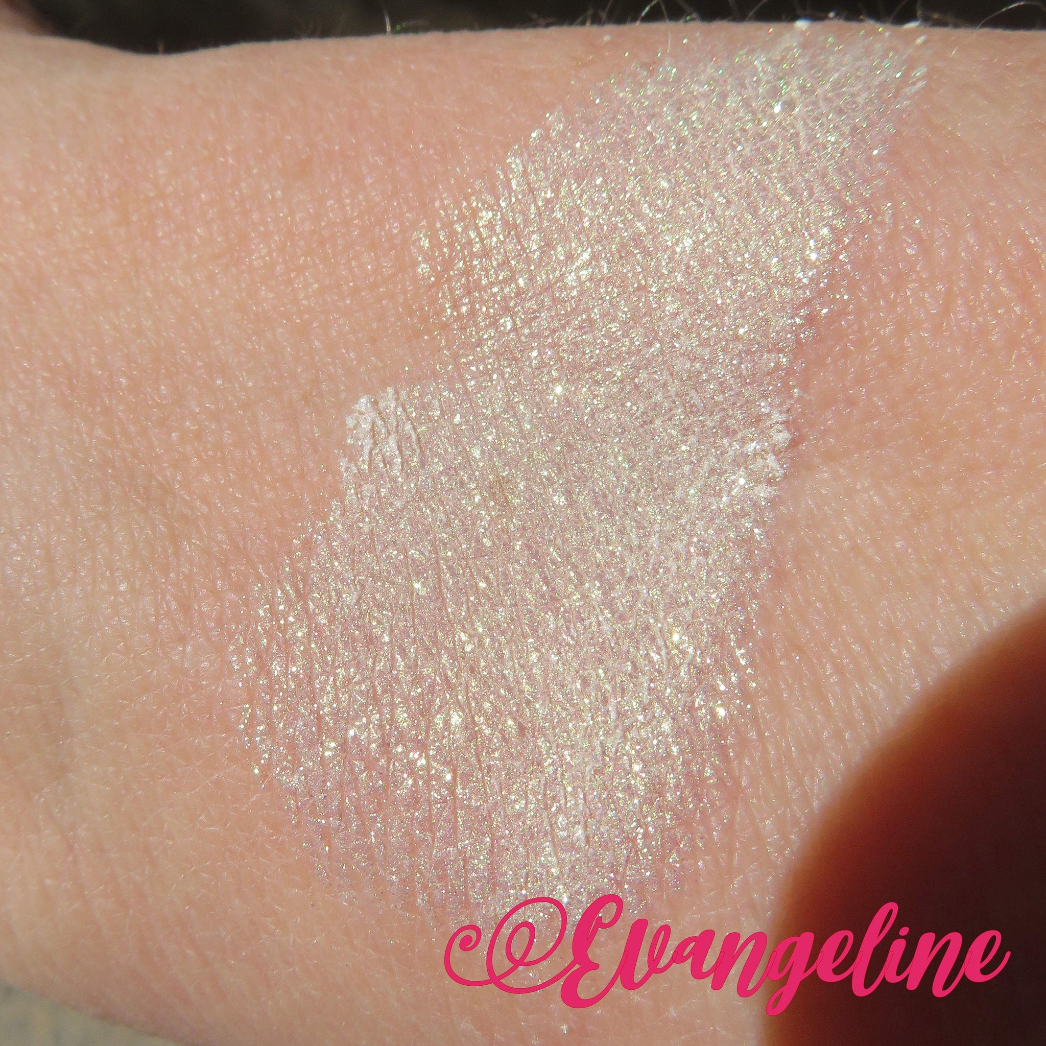 Side view of loose mineral eyeshadow in white shimmer with green gold sheen, showcasing fine powder texture