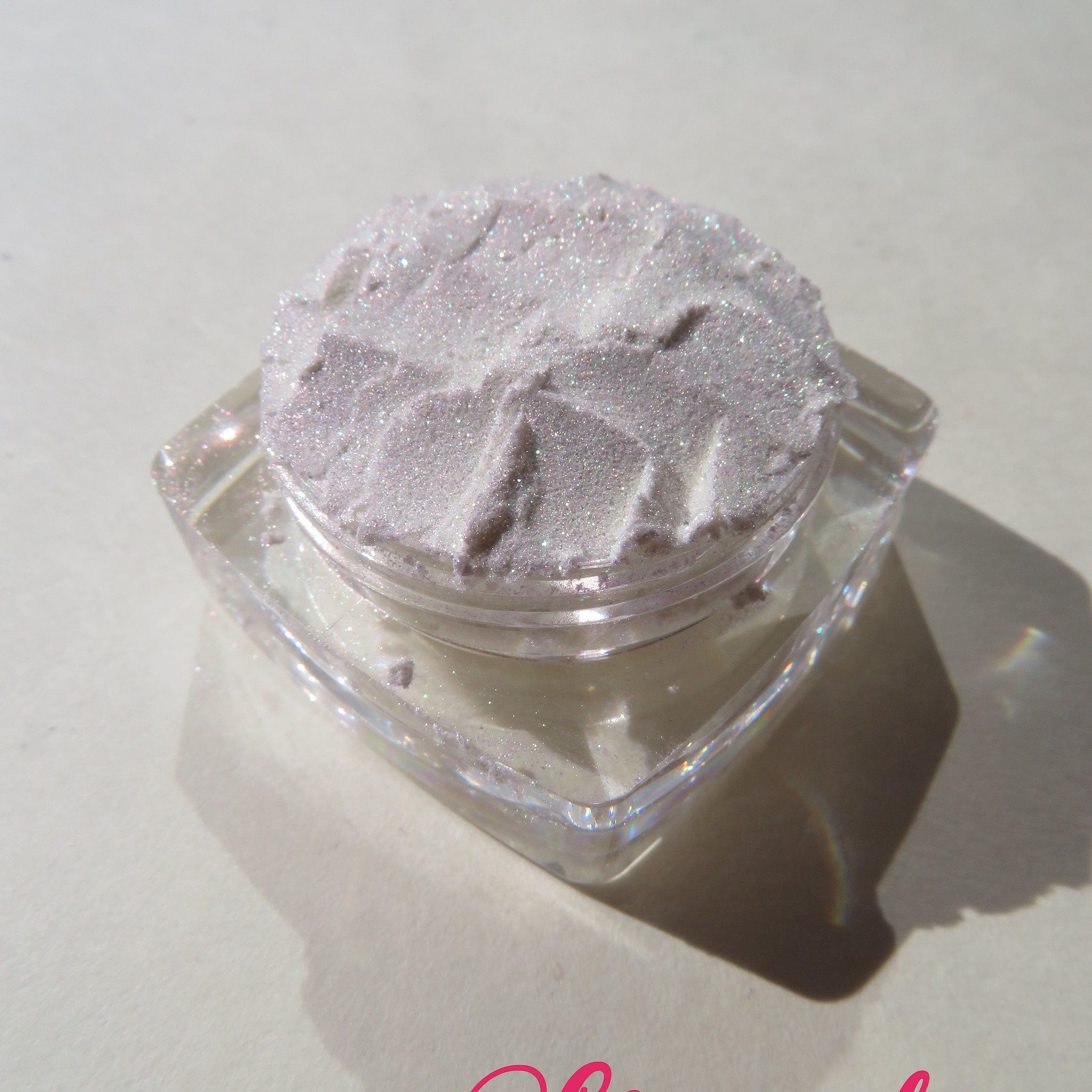 Side view of loose mineral eyeshadow in white shimmer with green gold sheen, showcasing its iridescent pigment texture.